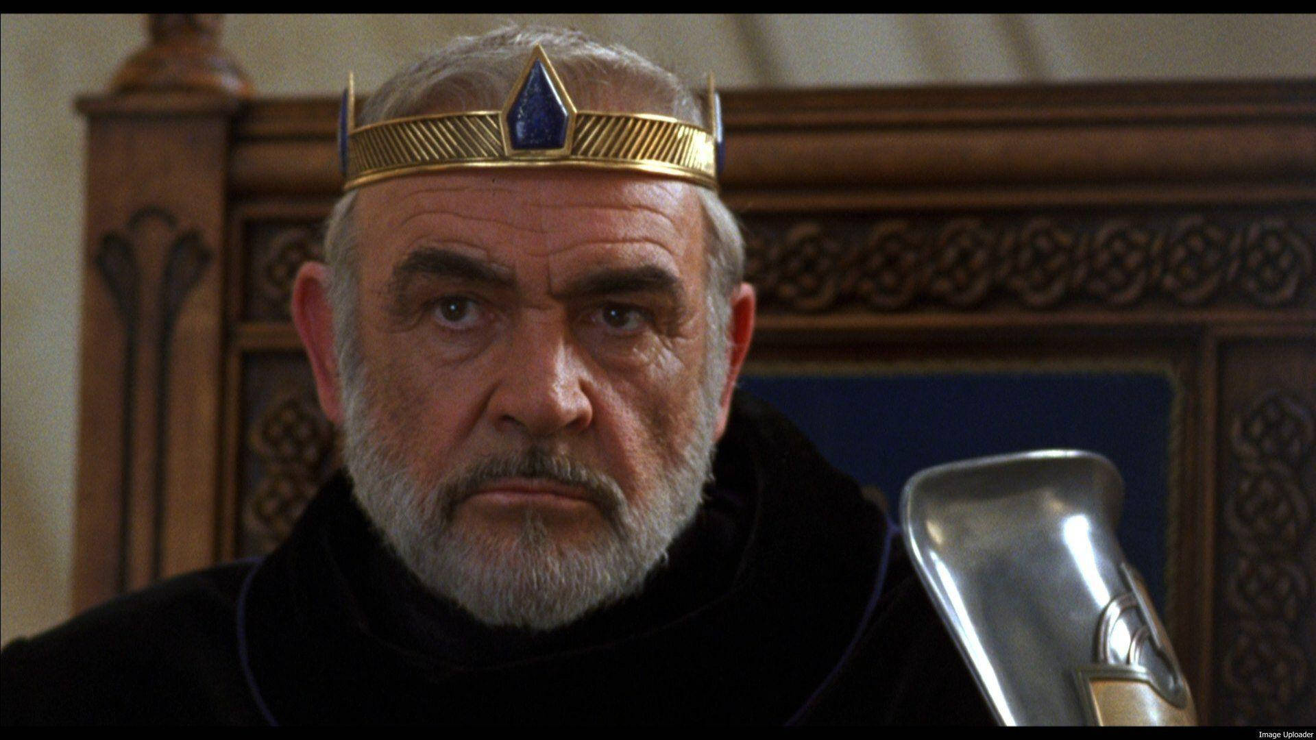 Sean Connery 桌布 壁紙 — 一位嚴肅的鬍鬚國王，戴著金色王冠和藍色寶石，從他華麗的王座上凝視著。