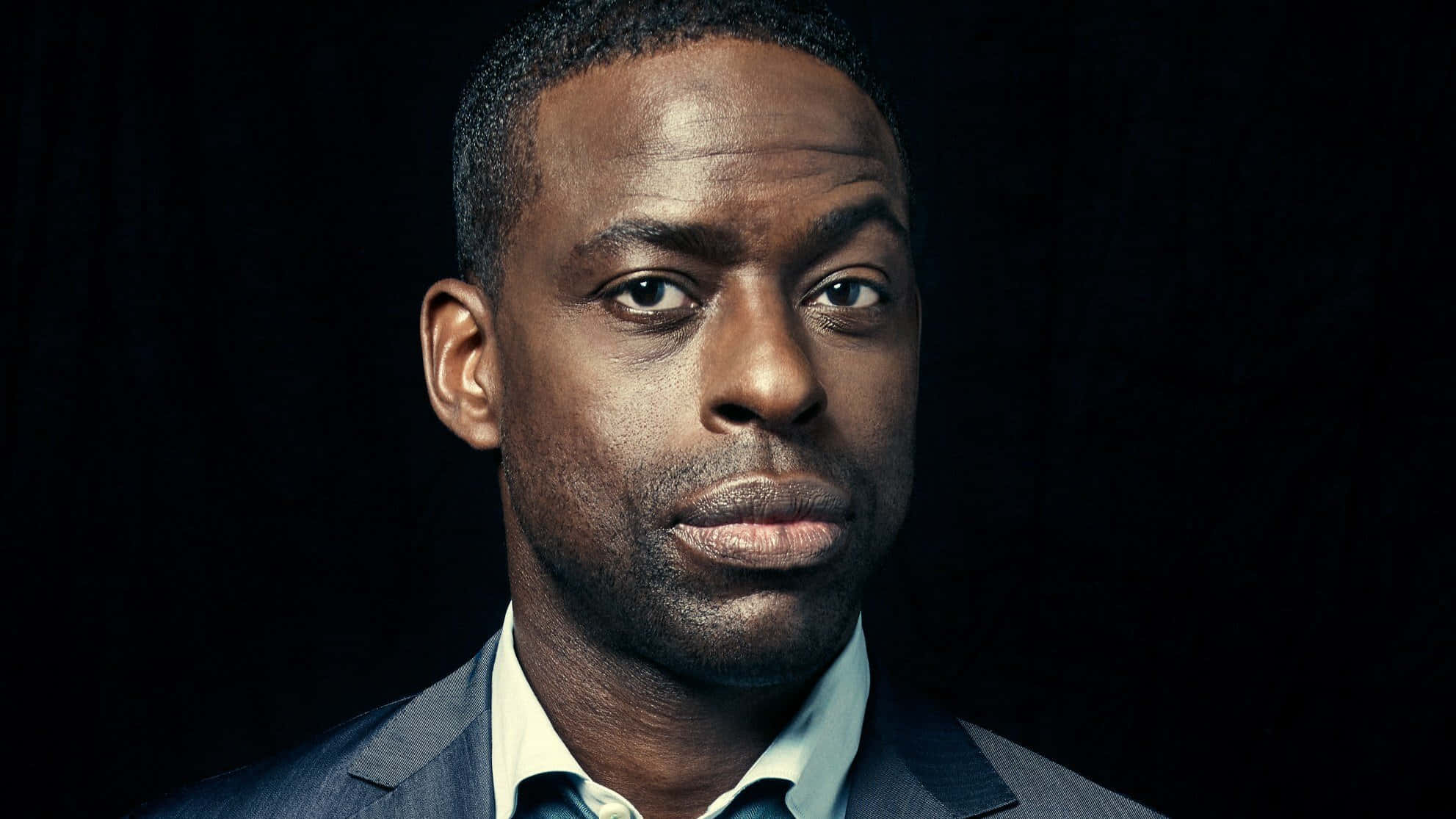 Sterling K Brown 桌布 壁紙 — 一位嚴肅的黑人男子穿著西裝，在黑暗背景下直視鏡頭。