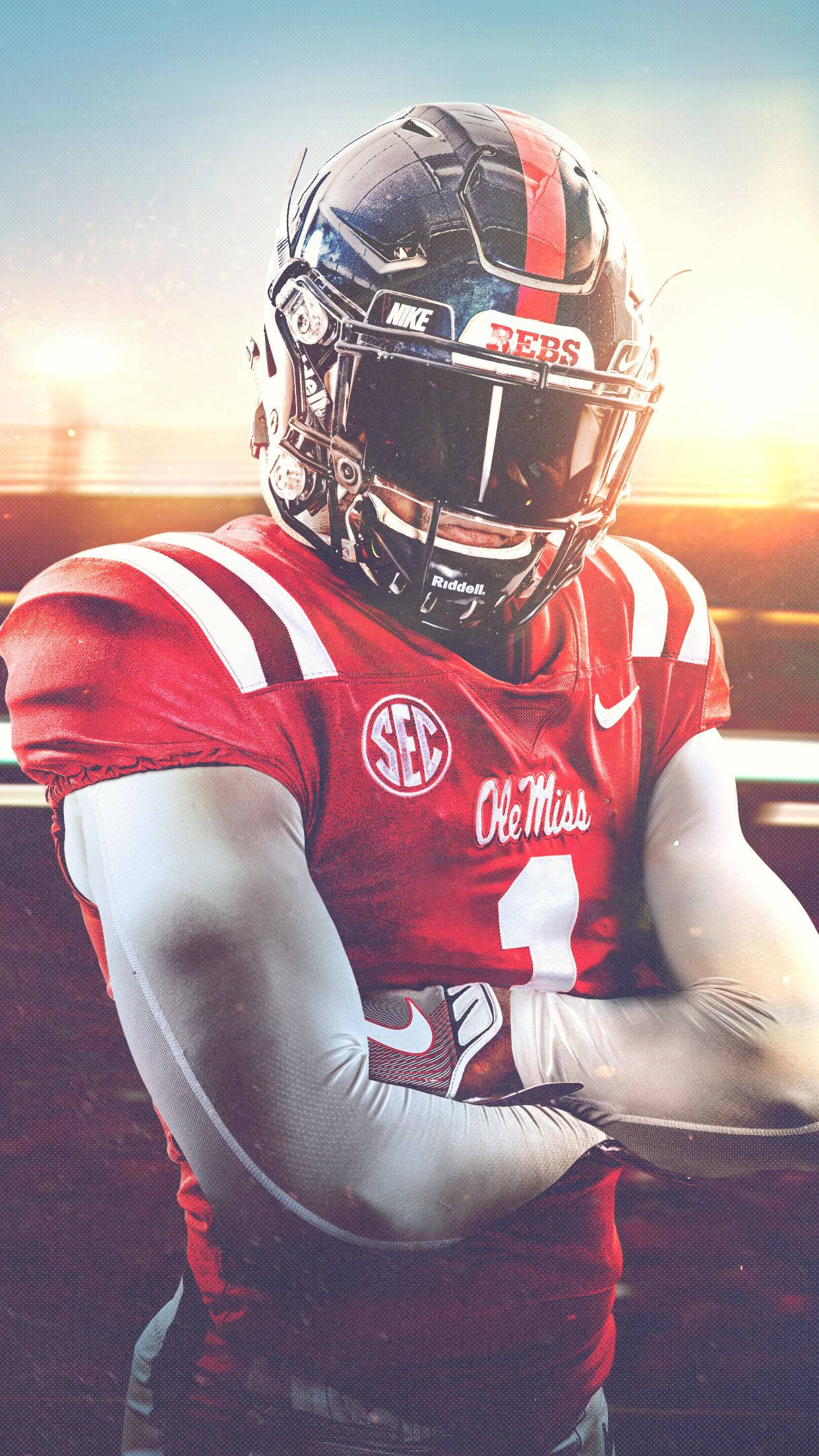 足球 桌布 壁紙 — 一位堅定的 Ole Miss 足球員，身穿紅白裝備，在燦爛的夕陽背景下交叉雙臂站立。