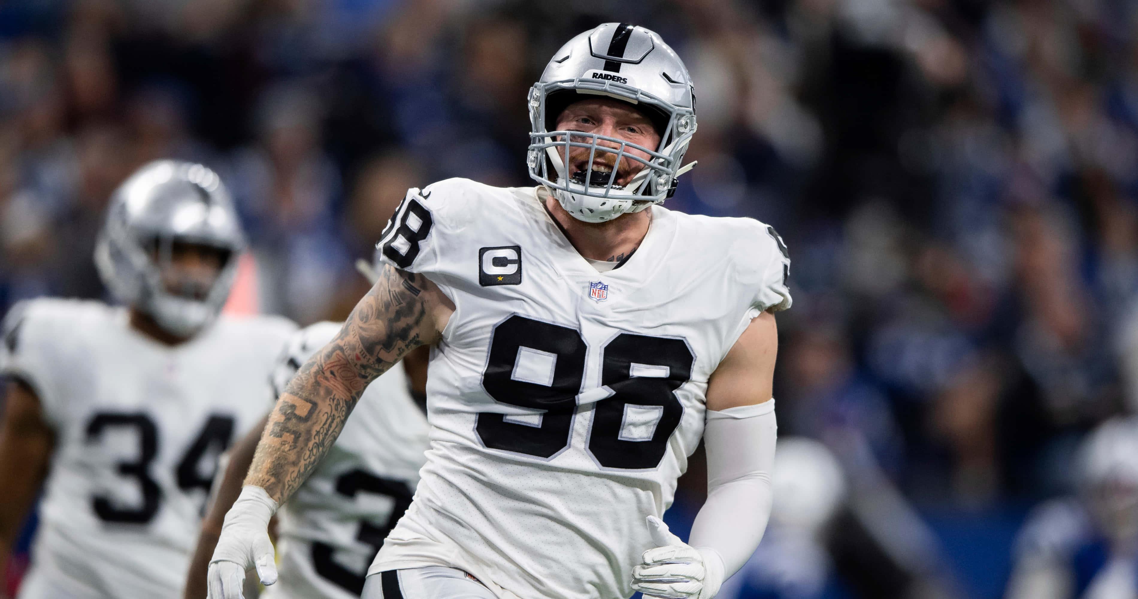 Las Vegas Raiders 桌布 壁紙 — 一位堅定的NFL球員身穿白色球衣，號碼98，在球場燈光下於比賽中衝刺穿過場地。