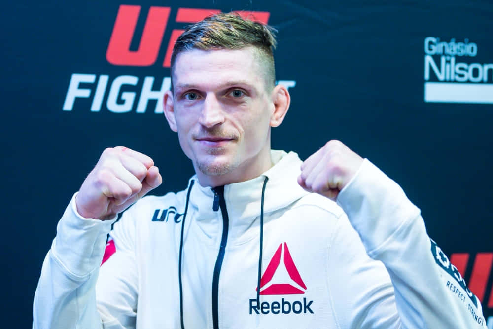MMA 桌布 壁紙 — 一位堅定的UFC拳手身穿白色Reebok連帽衫，在品牌背景前握緊拳頭擺姿勢。
