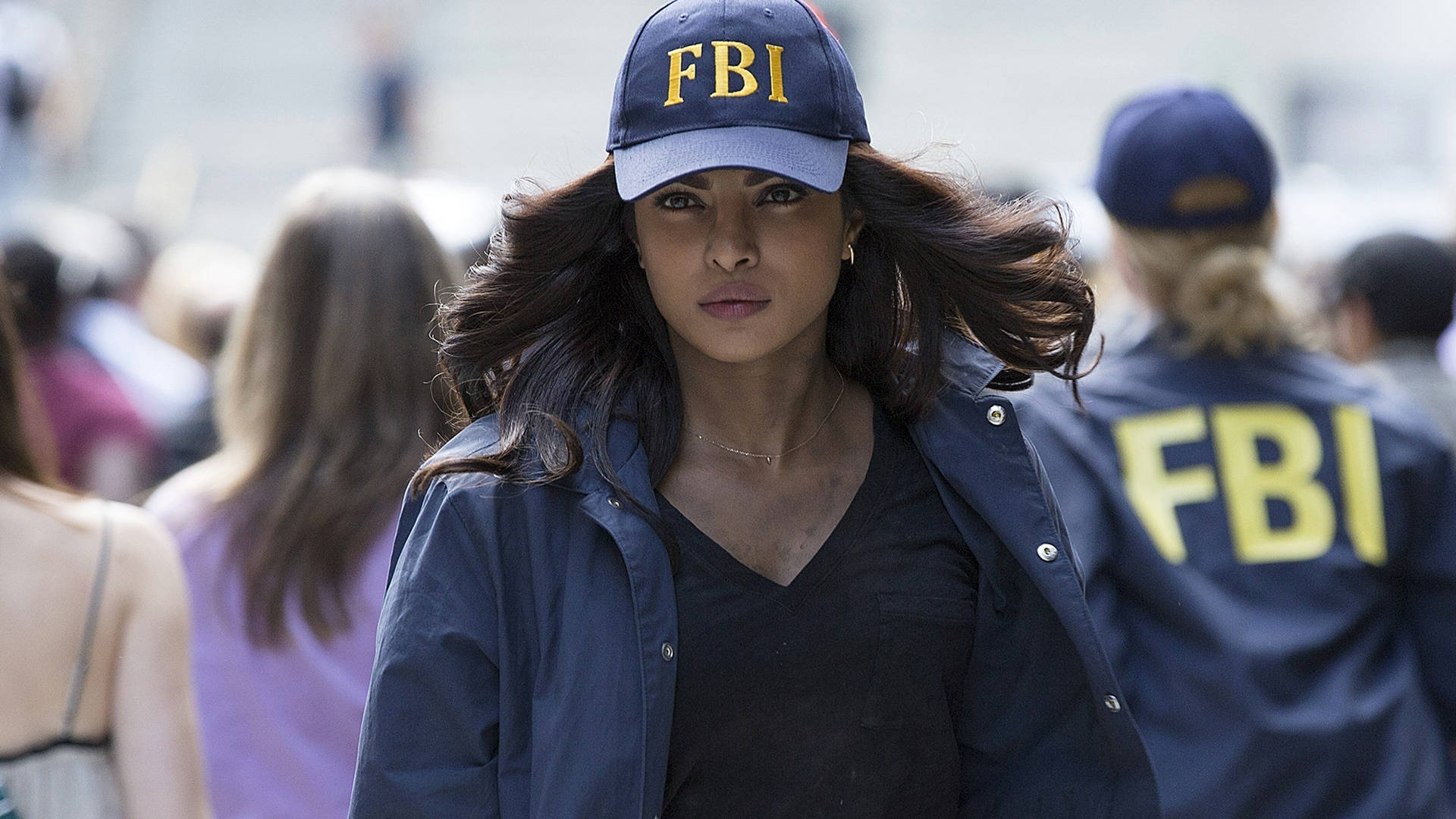 Fbi 桌布 壁紙 — 一位堅定的女性，戴著FBI帽子、穿著FBI外套，在風中飄揚的頭髮下，大步穿過熙攘的人群。