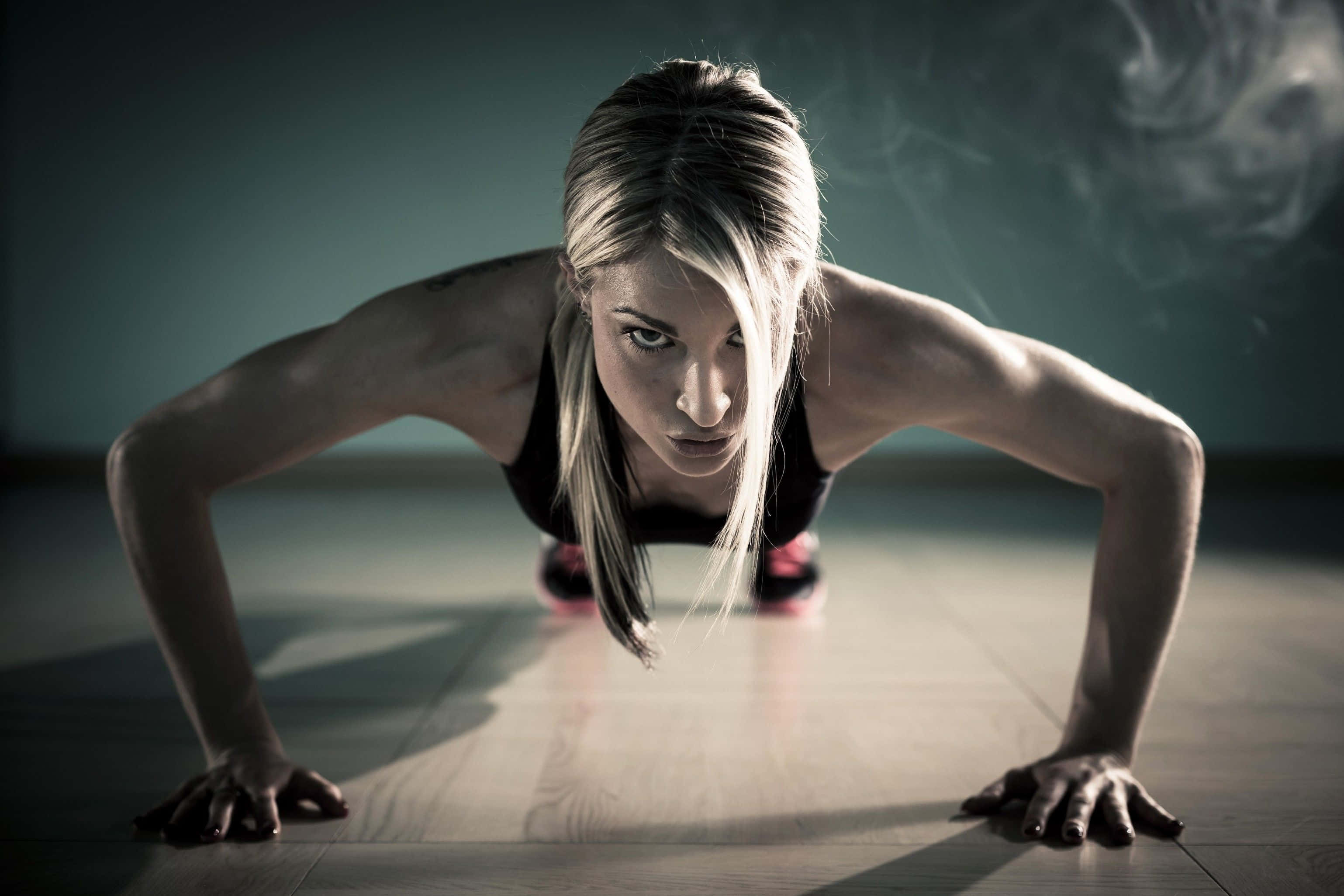 Workout 桌布 壁紙 — 一位堅定的女性在燈光昏暗的攝影棚中，專注地做伏地挺身，身後煙霧繚繞。