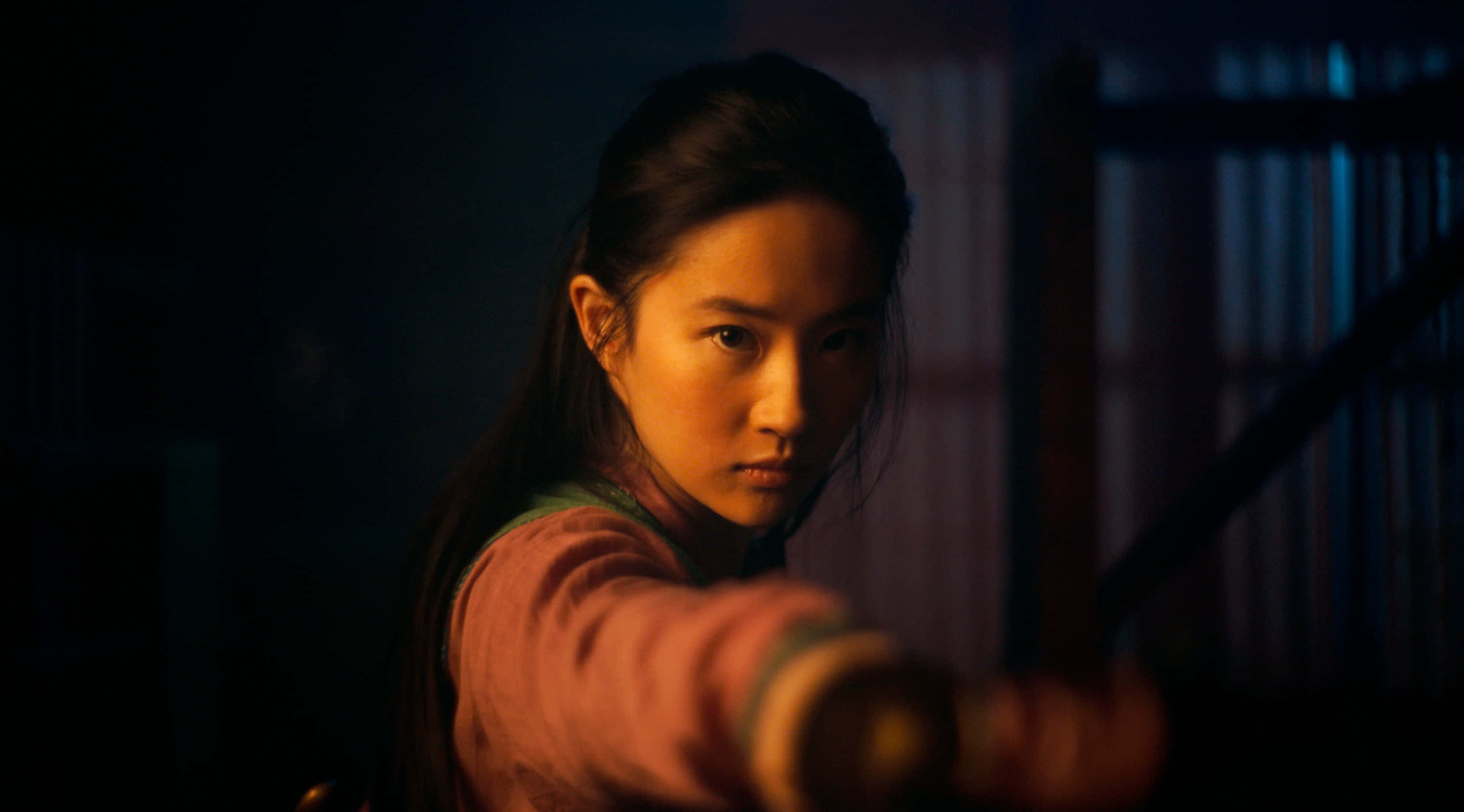 Mulan 桌布 壁紙 — 一位堅定的女戰士在昏暗光線下，在傳統環境中專注地將劍向前伸出。