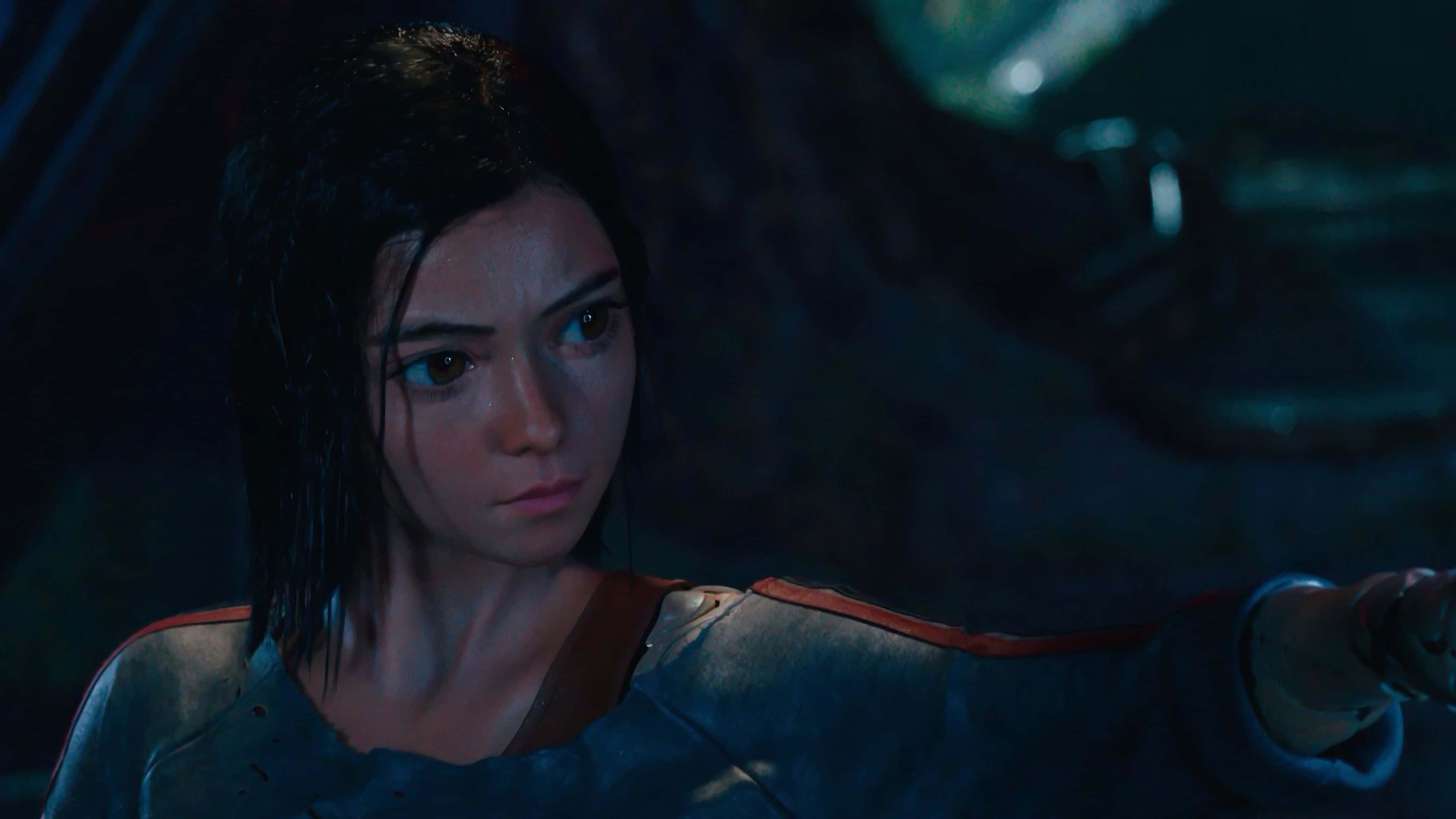 Alita Battle Angel 桌布 壁紙 — 一位堅定的女戰士身穿暗色盔甲，在昏暗的藍色燈光下，於陰暗的未來場景中緊握一把劍。