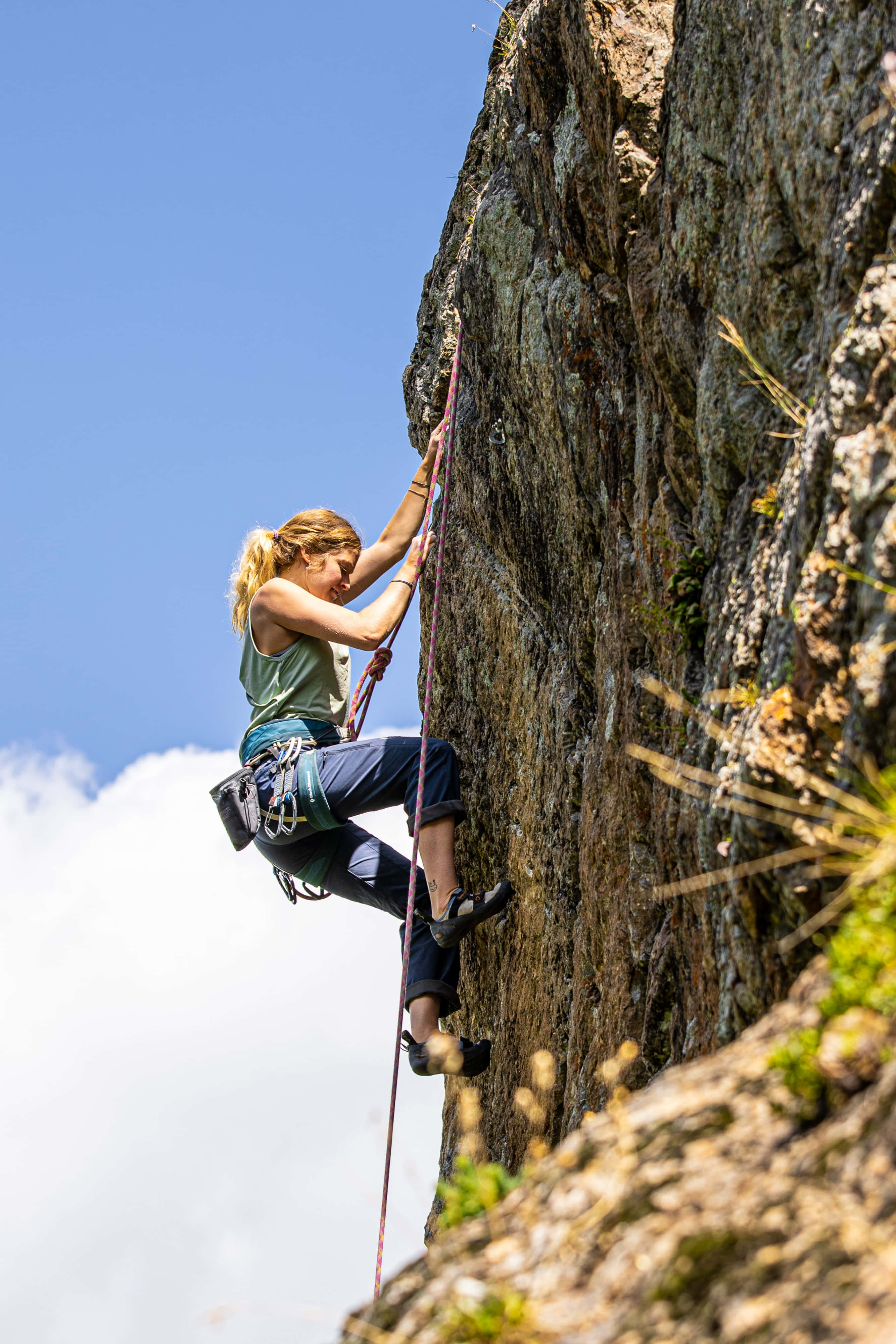 Climbing 桌布 壁紙 — 一位堅定的女攀岩者在明亮的藍天和蓬鬆的白雲下攀登崎嶇的岩壁。