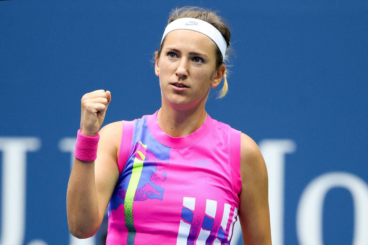 Athletic 桌布 壁紙 — 一位堅定的女網球選手穿著充滿活力的粉紅色和藍色運動服，在純藍色球場背景下握拳慶祝勝利。