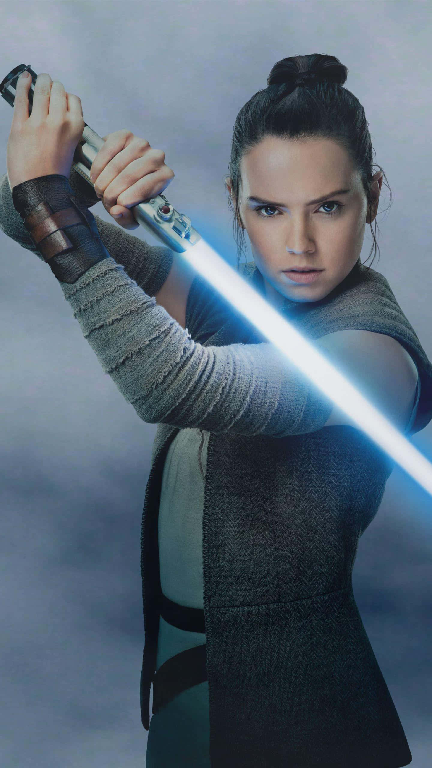 Rey Star Wars 桌布 壁紙 — 一位堅定的年輕女子在霧濛濛的灰色背景下，專注地揮舞著發光的藍色光劍。