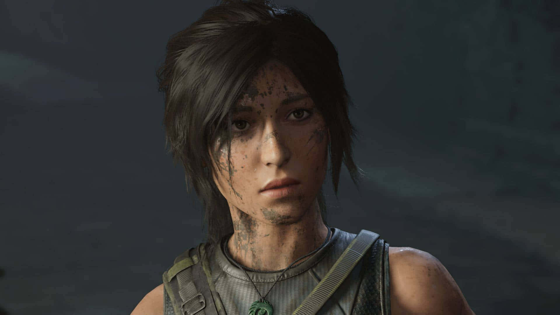 Best Shadow Of The Tomb Raider 桌布 壁紙 — 一位堅定的年輕探險家，臉上沾滿污垢，裝備粗獷，在黑暗模糊的背景中專注地凝視。