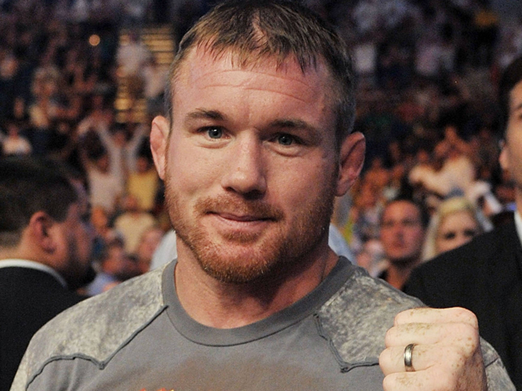 UFC 桌布 壁紙 — 一位堅定的戰士，握緊拳頭，目光專注，站在明亮競技場中模糊的人群前。