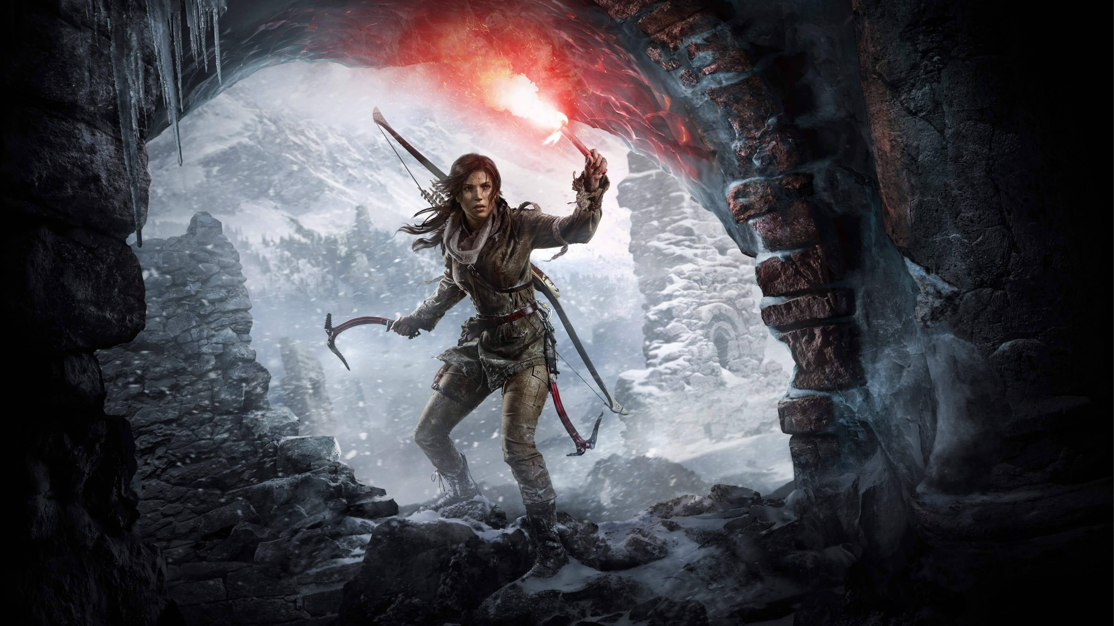 Tomb Raider Game 桌布 壁紙 — 一位堅定的探險家手持燃燒的火把和攀岩裝備，從一個積雪的洞穴入口走進霧氣瀰漫的山地景觀。