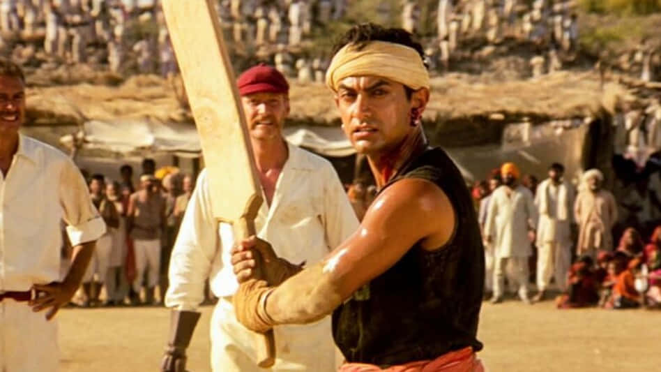 Aamir Khan 桌布 壁紙 — 一位堅定的板球擊球手穿著傳統服裝，在塵土飛揚的鄉村體育場比賽中，專注地揮動球棒。