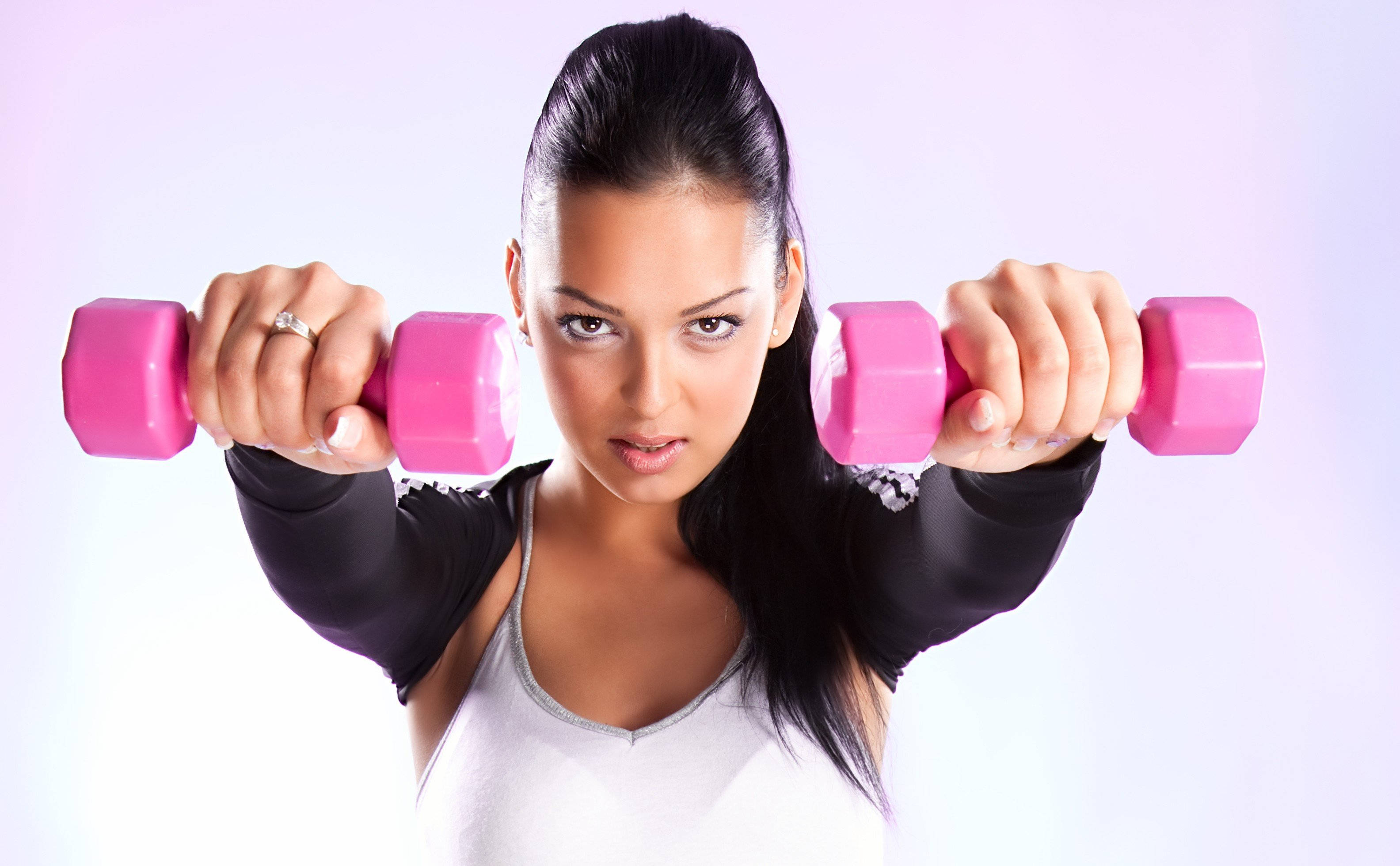 Barbell 桌布 壁紙 — 一位堅定的深色頭髮女性，在柔和的薰衣草背景前，將粉紅色啞鈴舉至肩高。