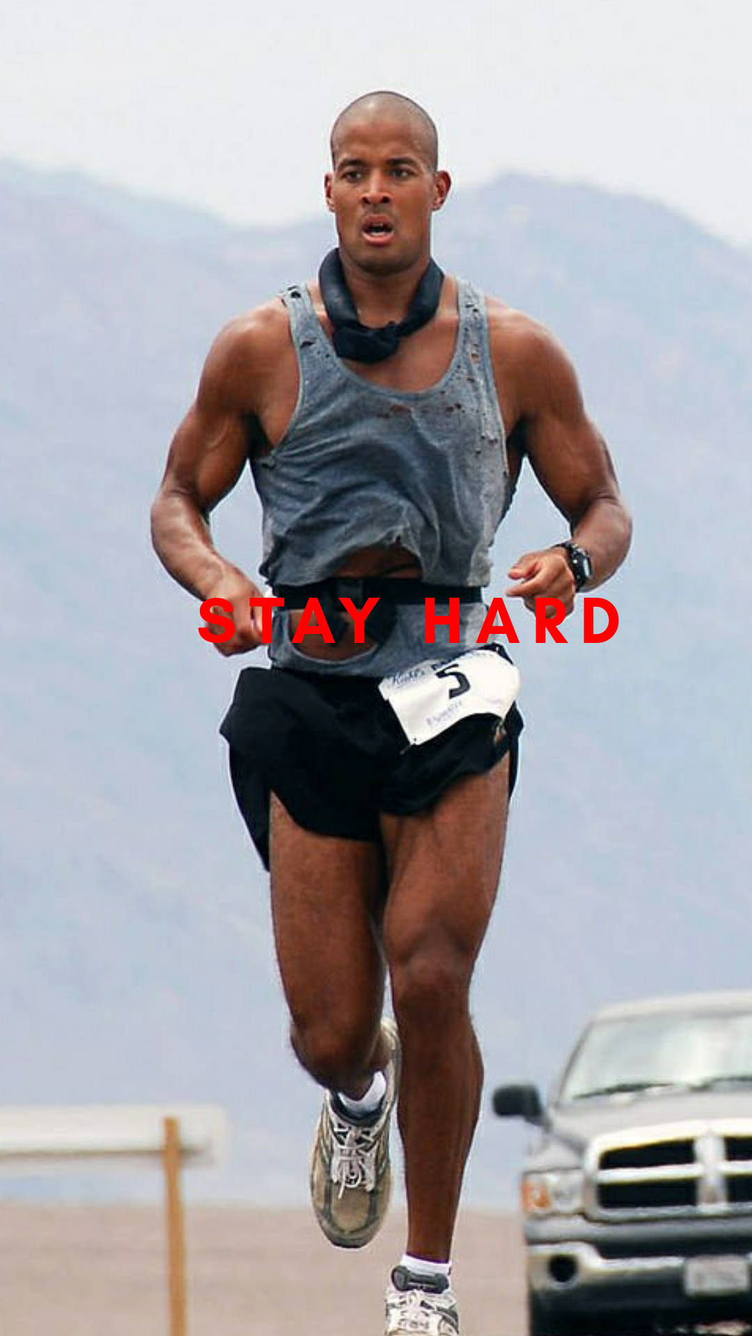 一位男性跑者在比賽中，胸前印有「STAY HARD」字樣，背景為山區地形。 — 勵志動圖 壁紙
