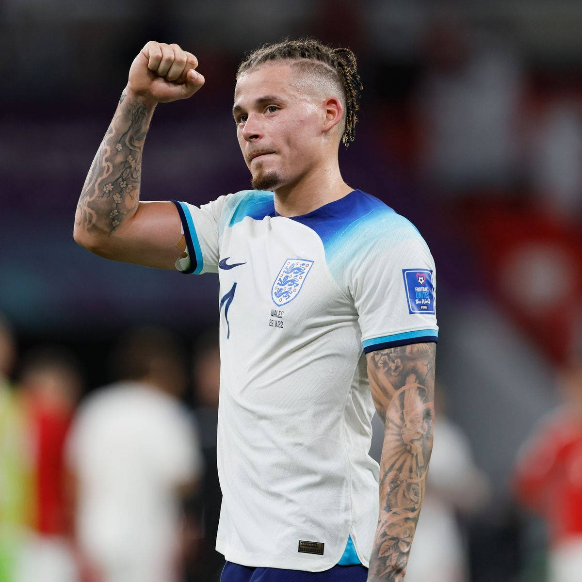 Football Players 桌布 壁紙 — 一位堅定的英格蘭足球員身穿帶有藍色點綴的白色球衣，手臂上有明顯的刺青，高舉拳頭慶祝勝利。