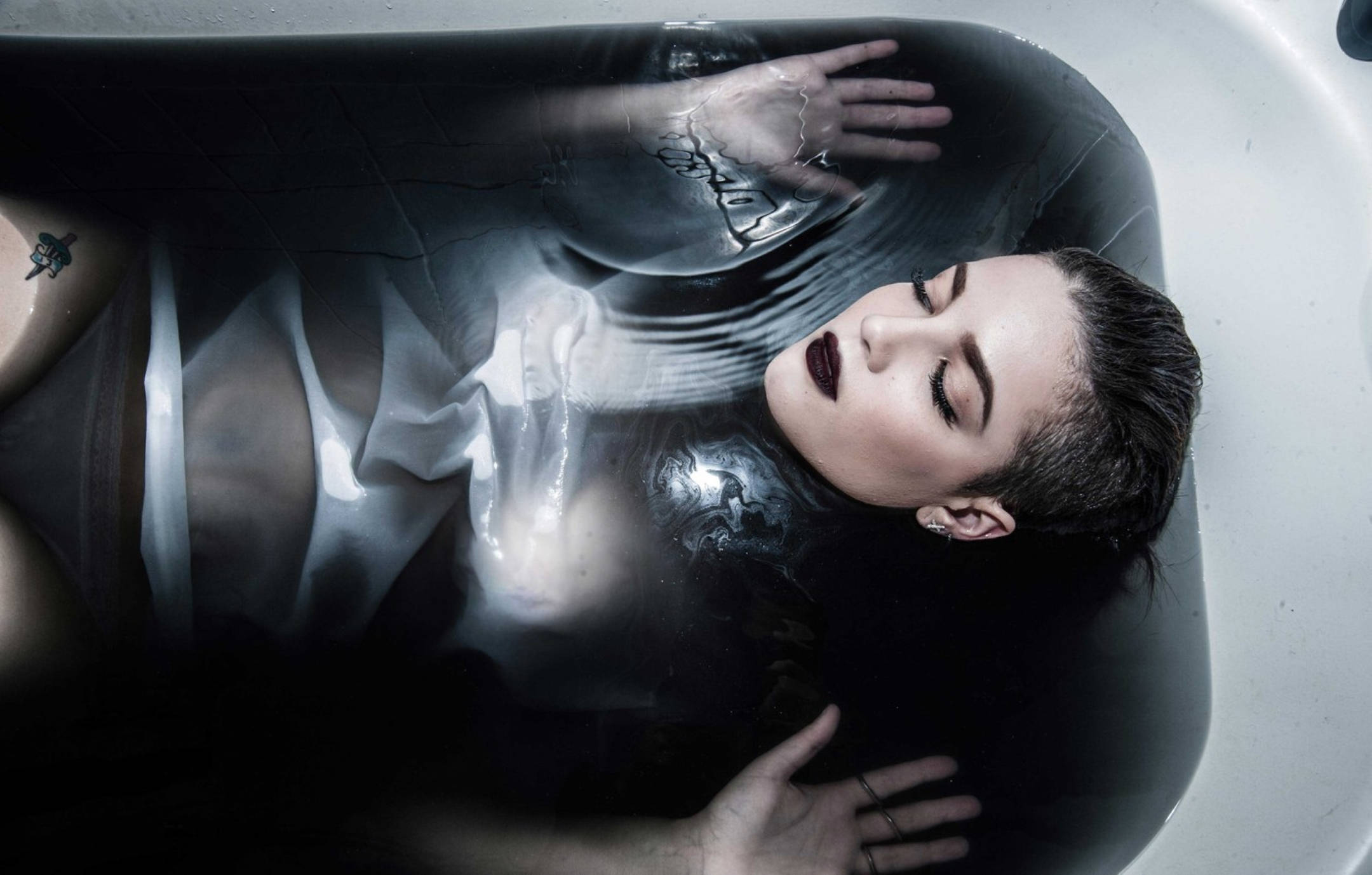 Halsey 桌布 壁紙 — 一位塗著深色口紅的女性，在注滿黑水的浴缸中寧靜地漂浮，雙手輕柔地放在水面上。