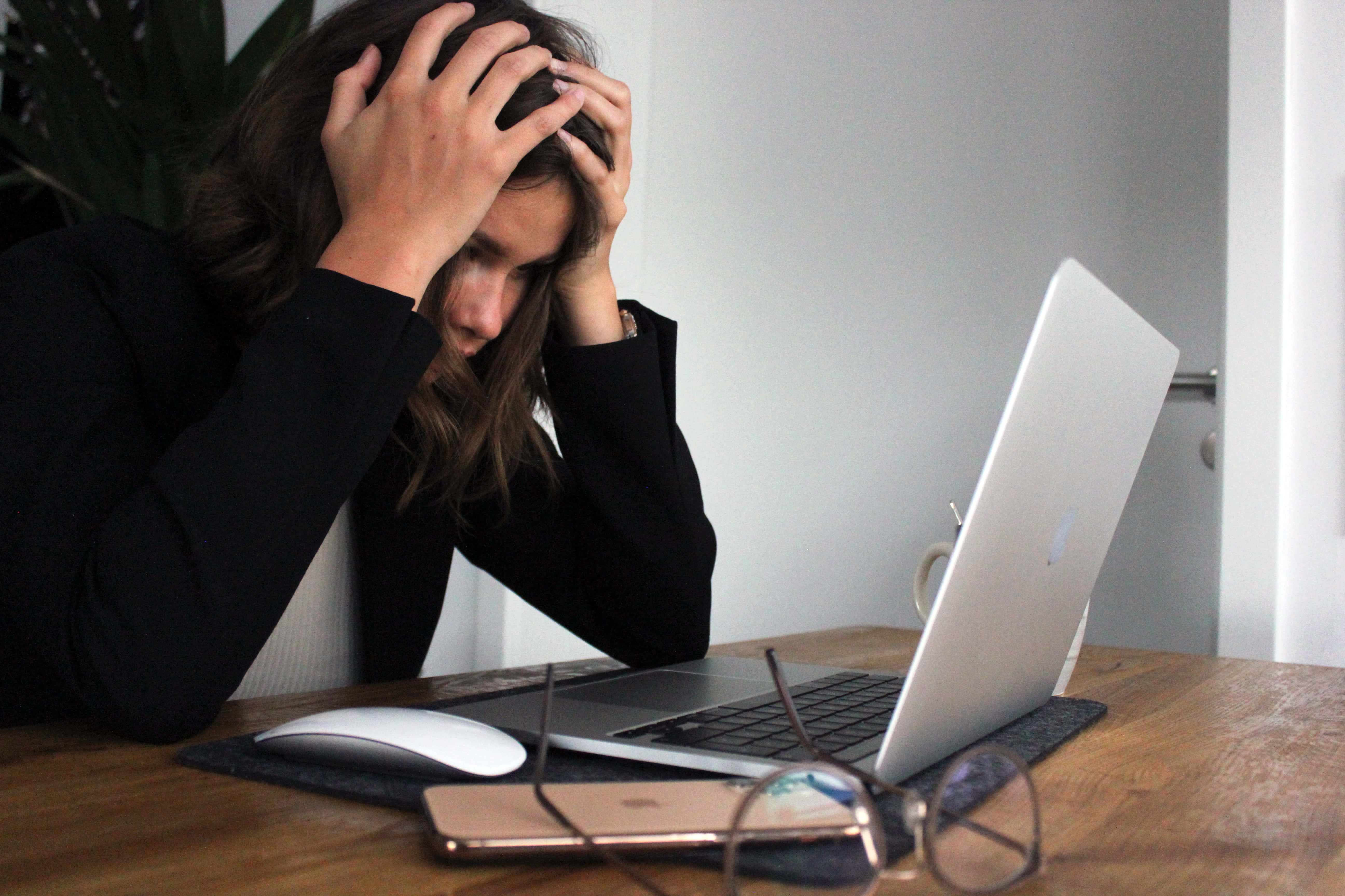 Stress 桌布 壁紙 — 一位壓力大的女士雙手放在頭上，俯身於現代室內環境中的木桌上使用筆記型電腦。