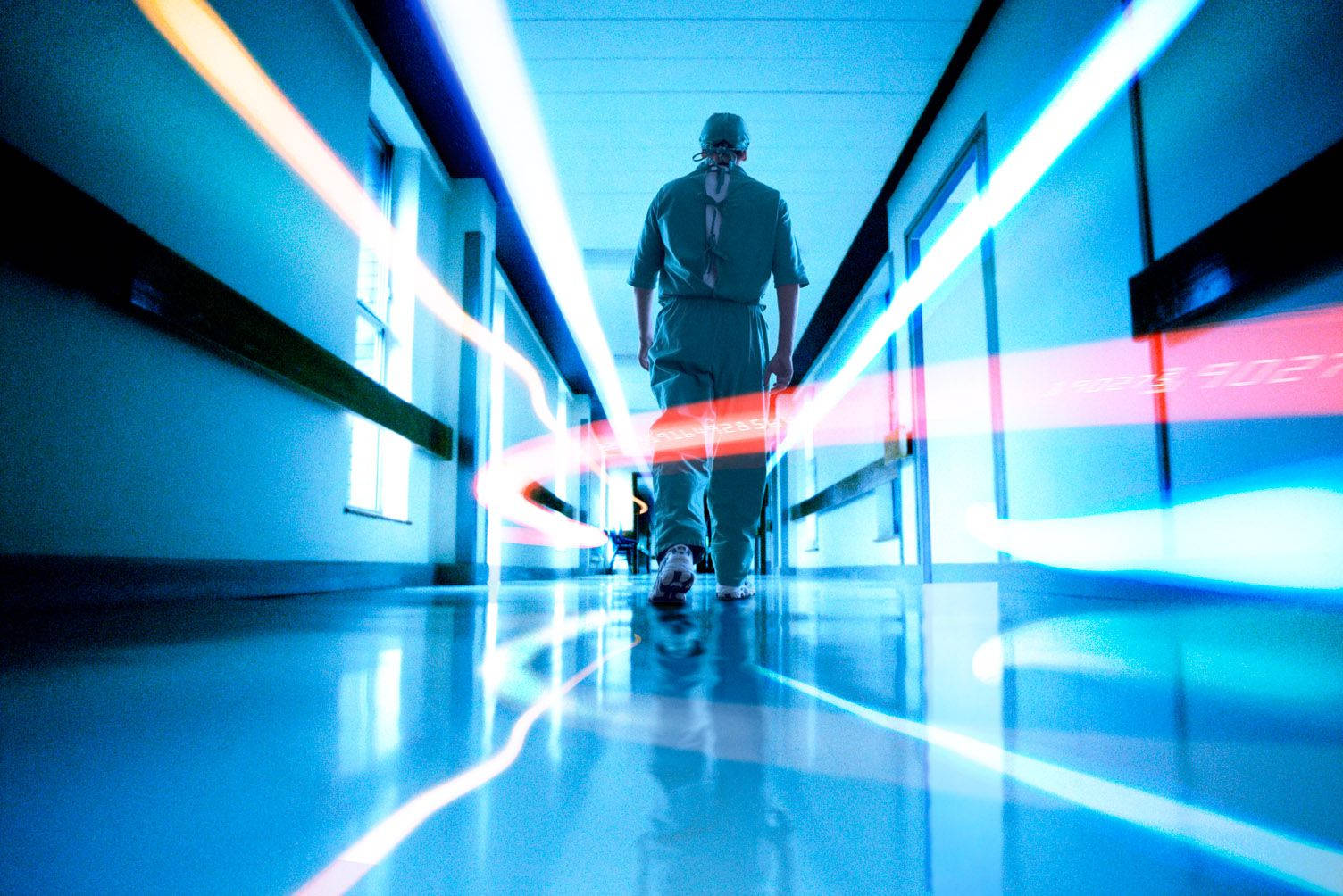 hallway 桌布 壁紙 — 一位外科醫生走在無菌的醫院走廊上，走廊被藍色和紅色的光跡照亮。