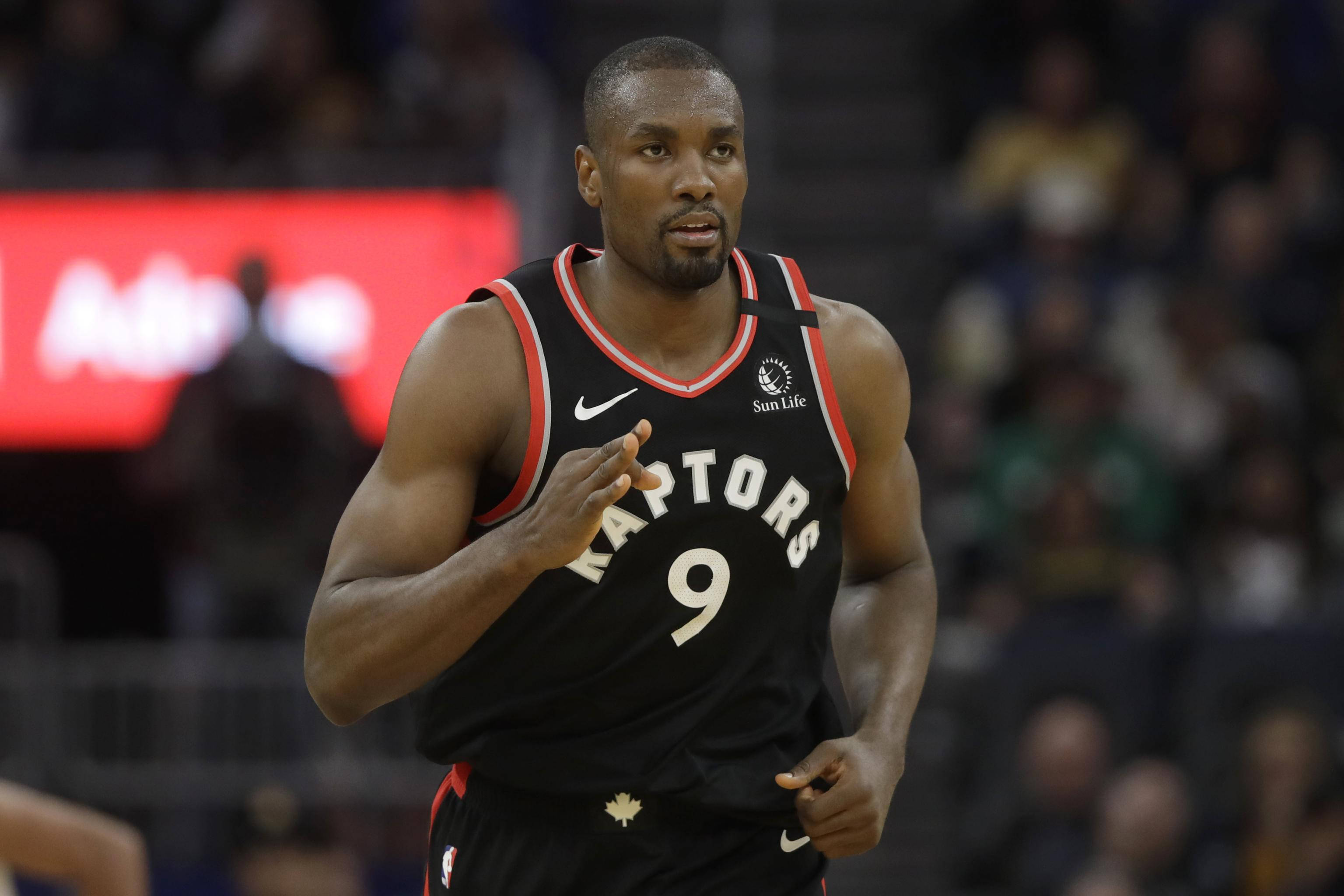 serge ibaka 桌布 壁紙 — 一位多倫多暴龍隊籃球運動員身穿黑色9號球衣，在明亮的場館燈光下於比賽中激烈奔跑。