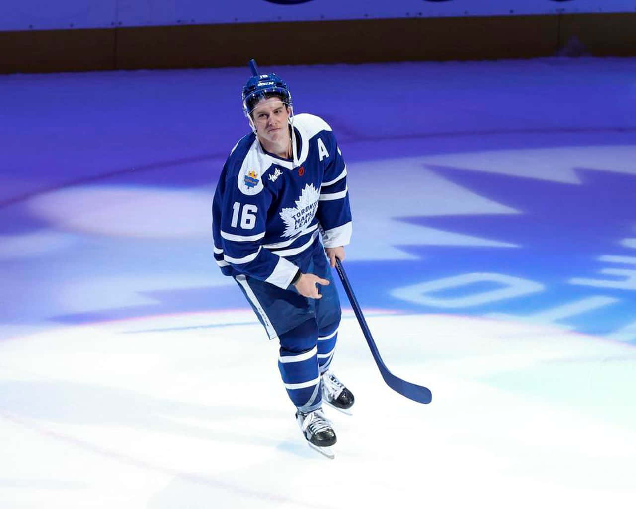 hockey 桌布 壁紙 — 一位多倫多楓葉隊的冰球運動員身穿藍白球衣，手持球桿在冰上滑行。