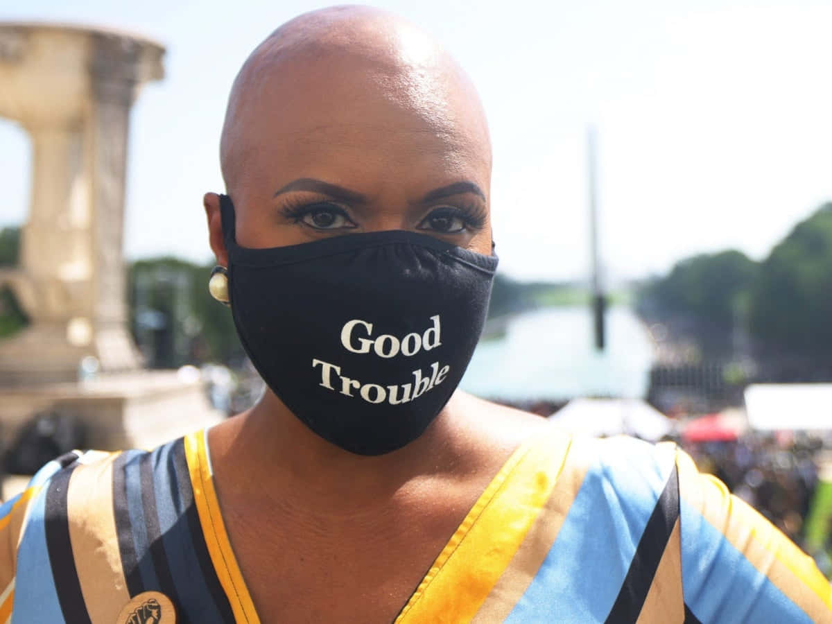 Mask 桌布 壁紙 — 一位大膽的光頭女性在明亮的戶外背景下戴著寫有「Good Trouble」的黑色口罩。
