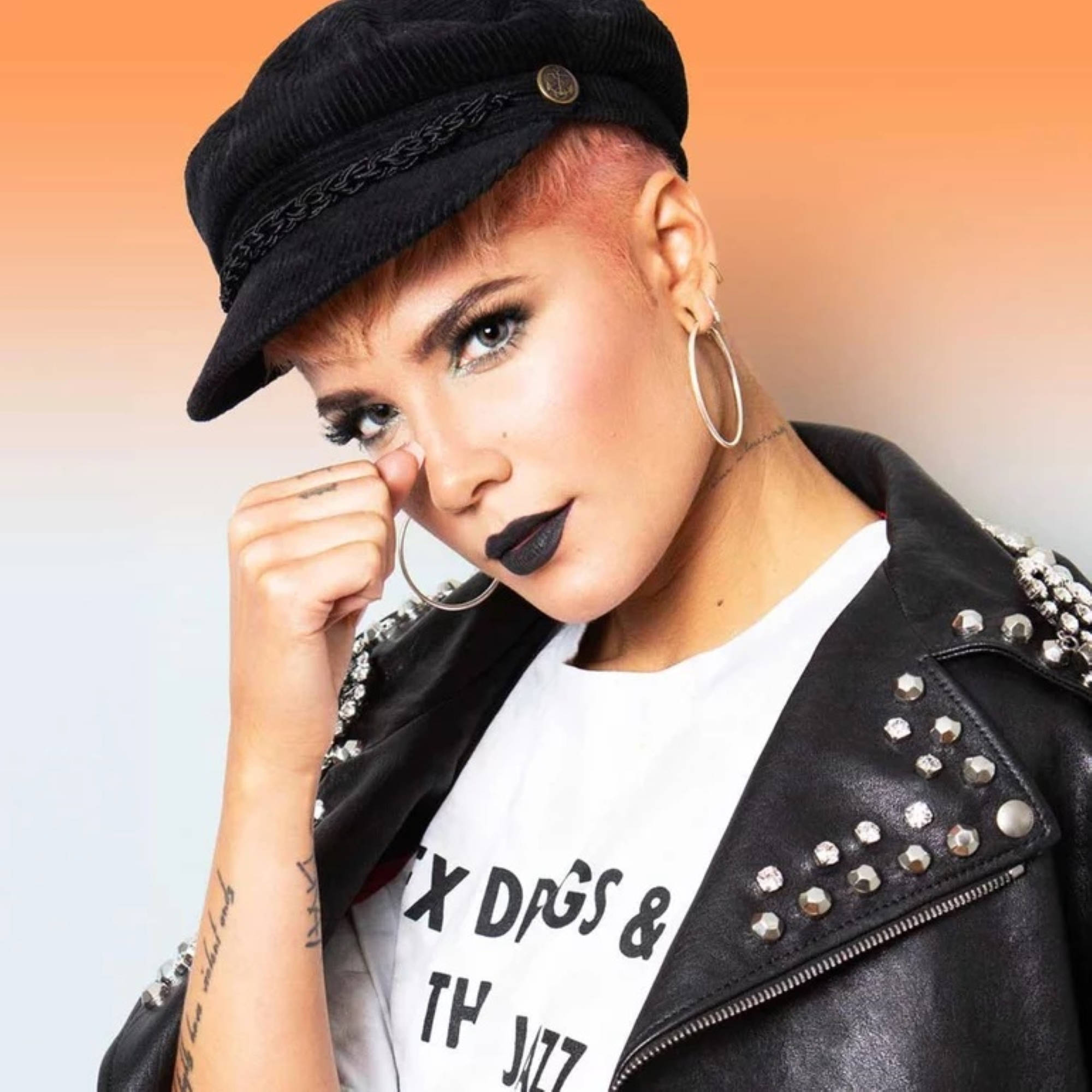 Halsey 桌布 壁紙 — 一位大膽的女性，粉紅色頭髮，戴黑色帽子，穿著鉚釘皮外套，在溫暖的漸變背景前自信地擺姿勢。