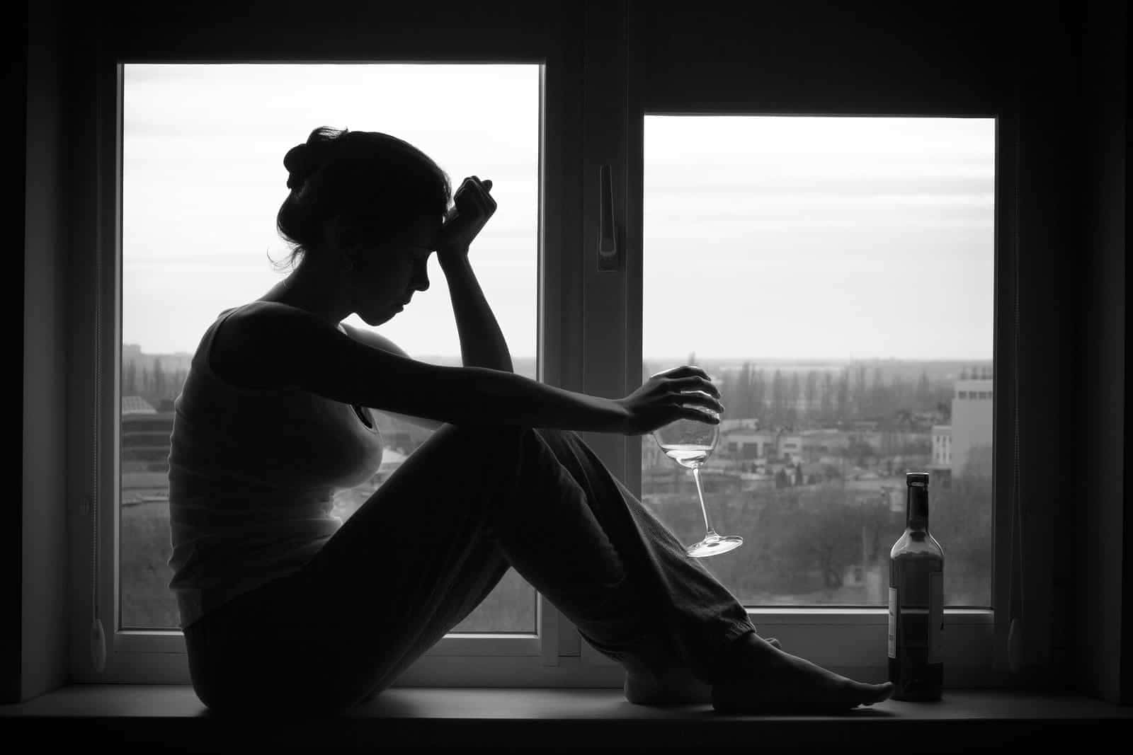 Depressed 桌布 壁紙 — 一位女士以剪影姿態坐在窗台上，手持酒杯，旁邊放著一瓶酒，俯瞰城市景觀。