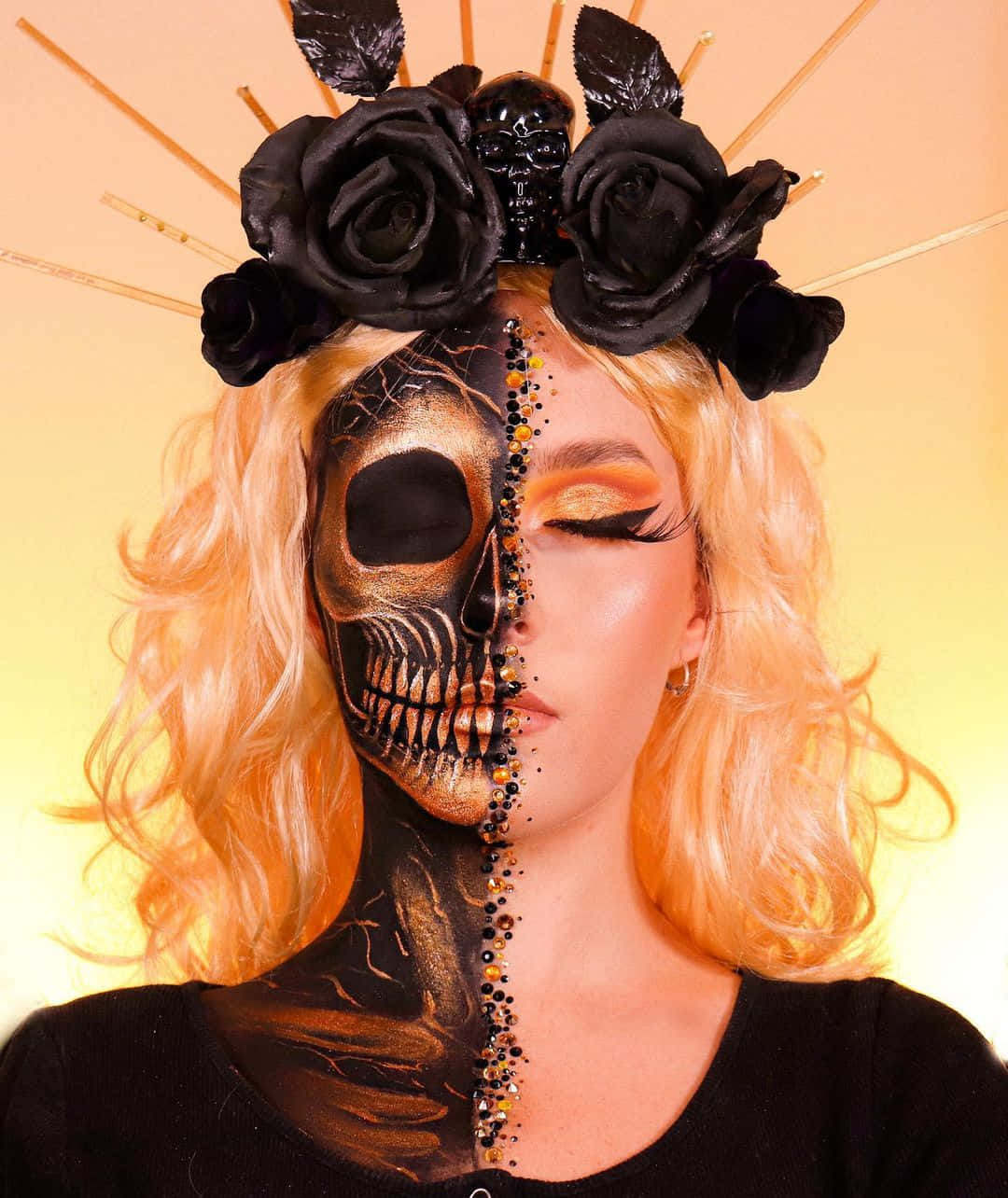 Halloween Makeup 桌布 壁紙 — 一位女士半邊臉被畫成金色骷髏，另一半是活生生的皮膚，飾有黑玫瑰和閃亮的尖刺，背景是溫暖的黃色。