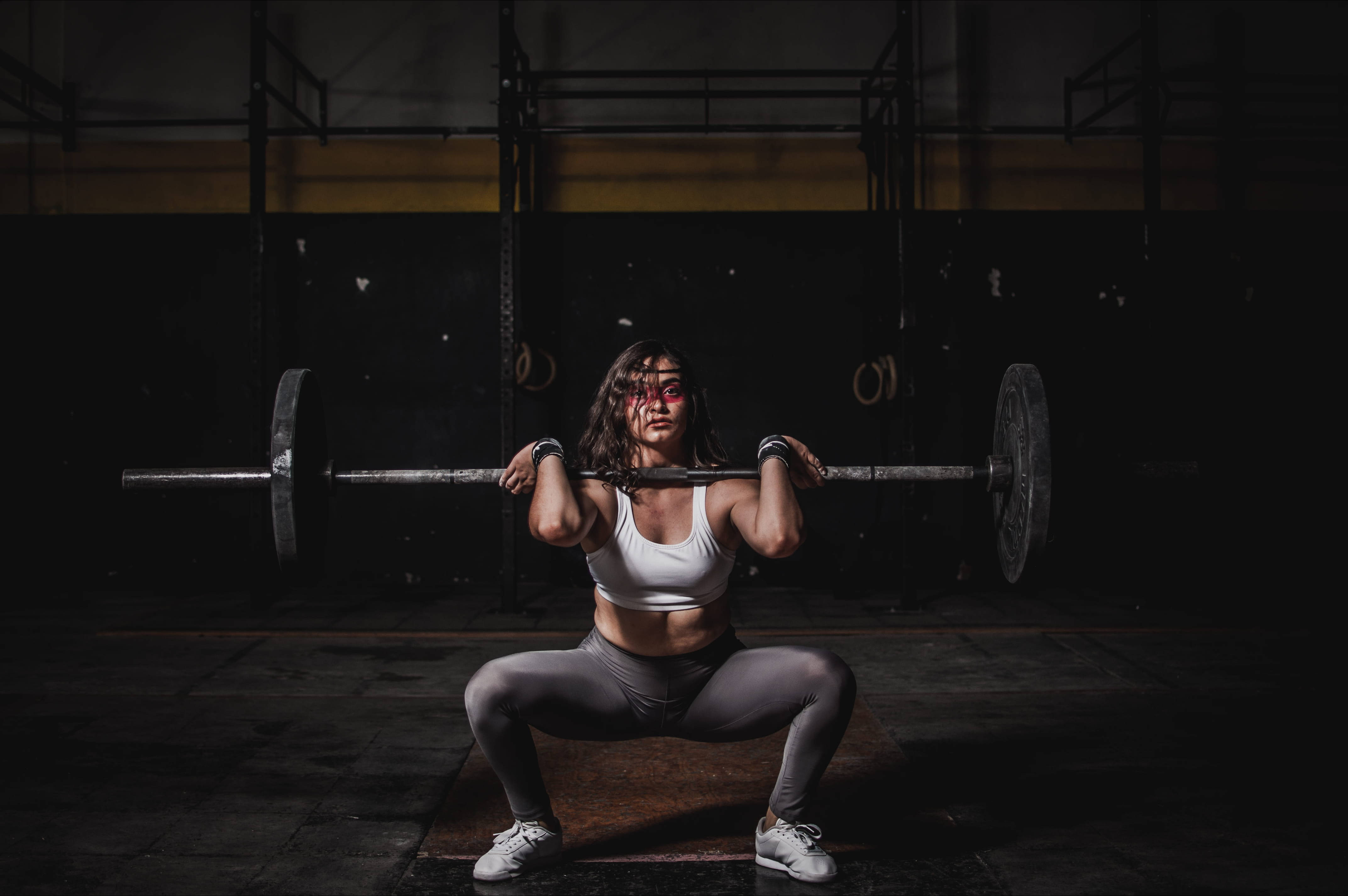 Barbell 桌布 壁紙 — 一位女士在健身房中，在戲劇性的聚光燈下，於深色背景前用槓鈴進行深蹲。