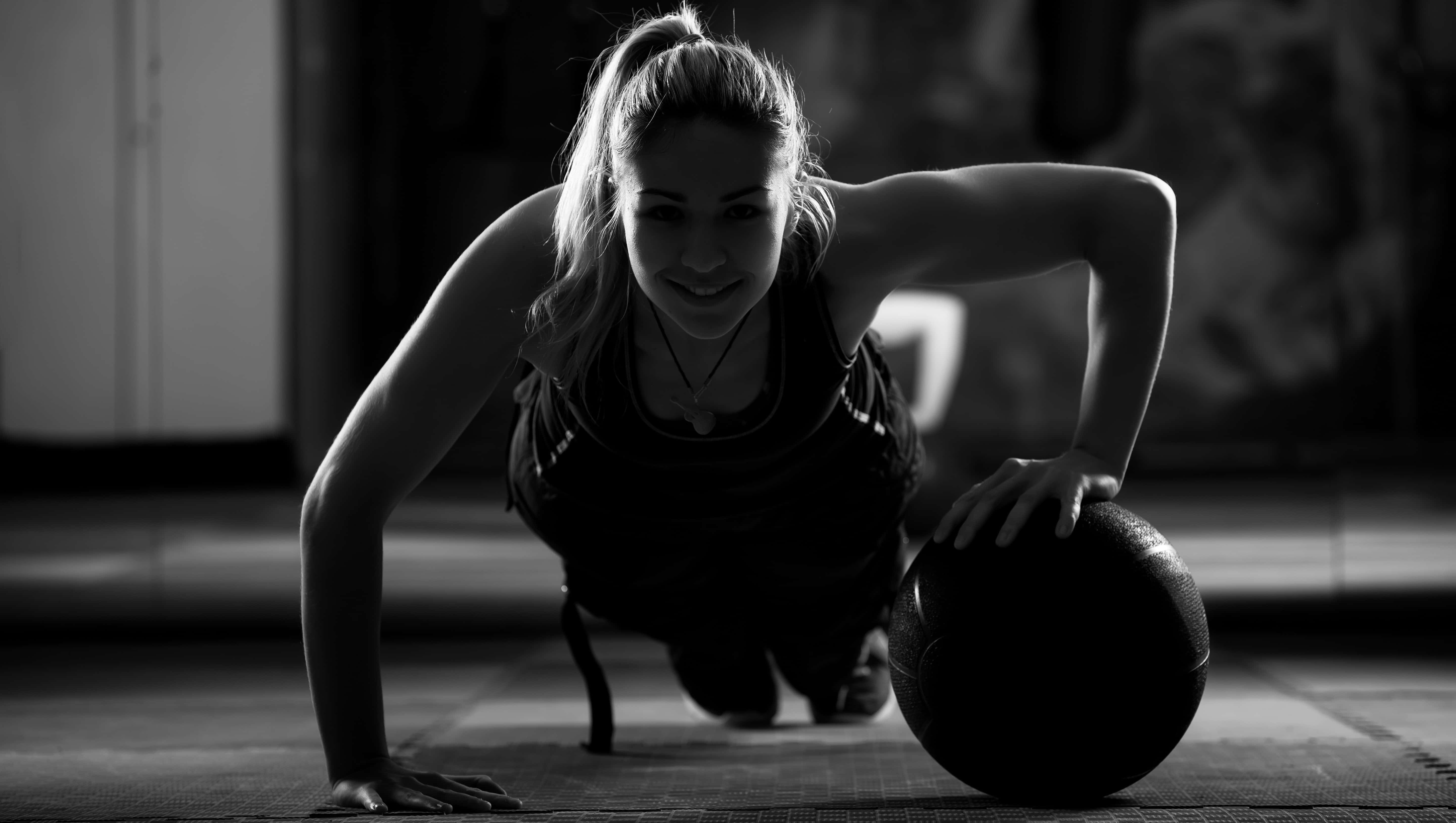 Fitness 桌布 壁紙 — 一位女士在健身房微笑著，同時以伏地挺身姿勢拿著藥球。