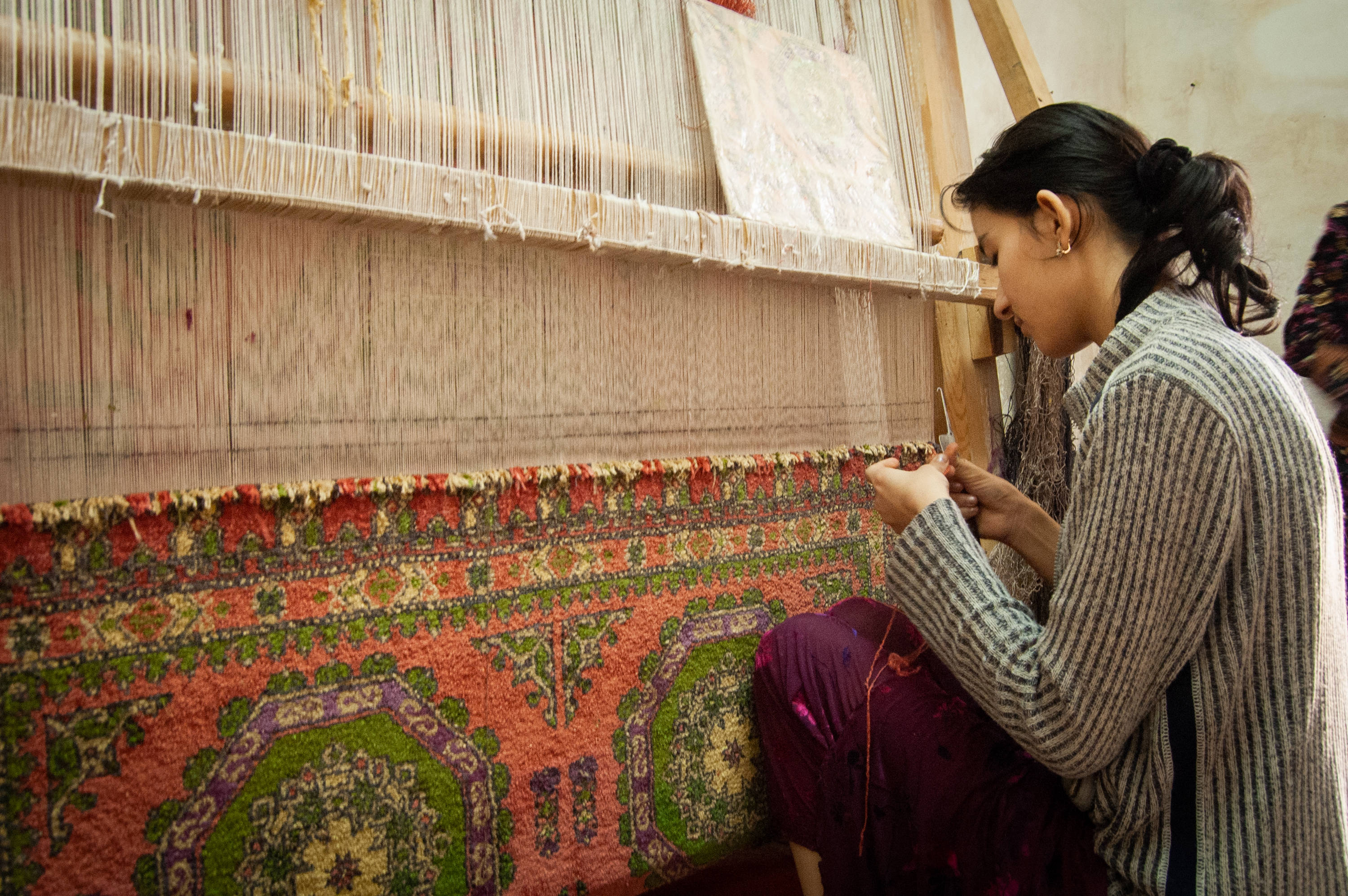 Uzbekistan 桌布 壁紙 — 一位女士在傳統織布機上專注精準地編織色彩鮮豔的圖案地毯。