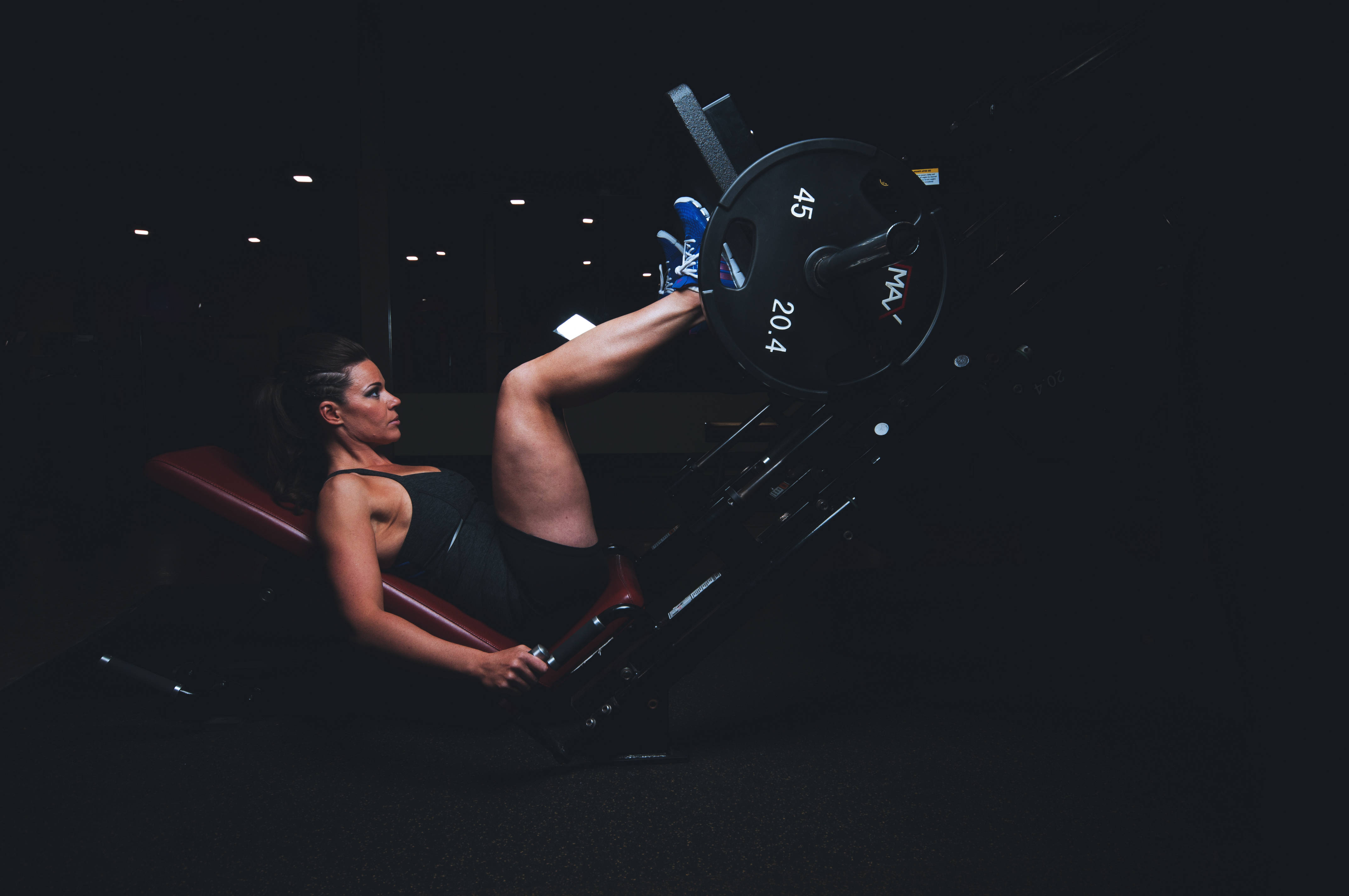 Fitness 桌布 壁紙 — 一位女士在光線昏暗的健身房中，專注地使用腿部推舉機舉起45磅槓鈴。