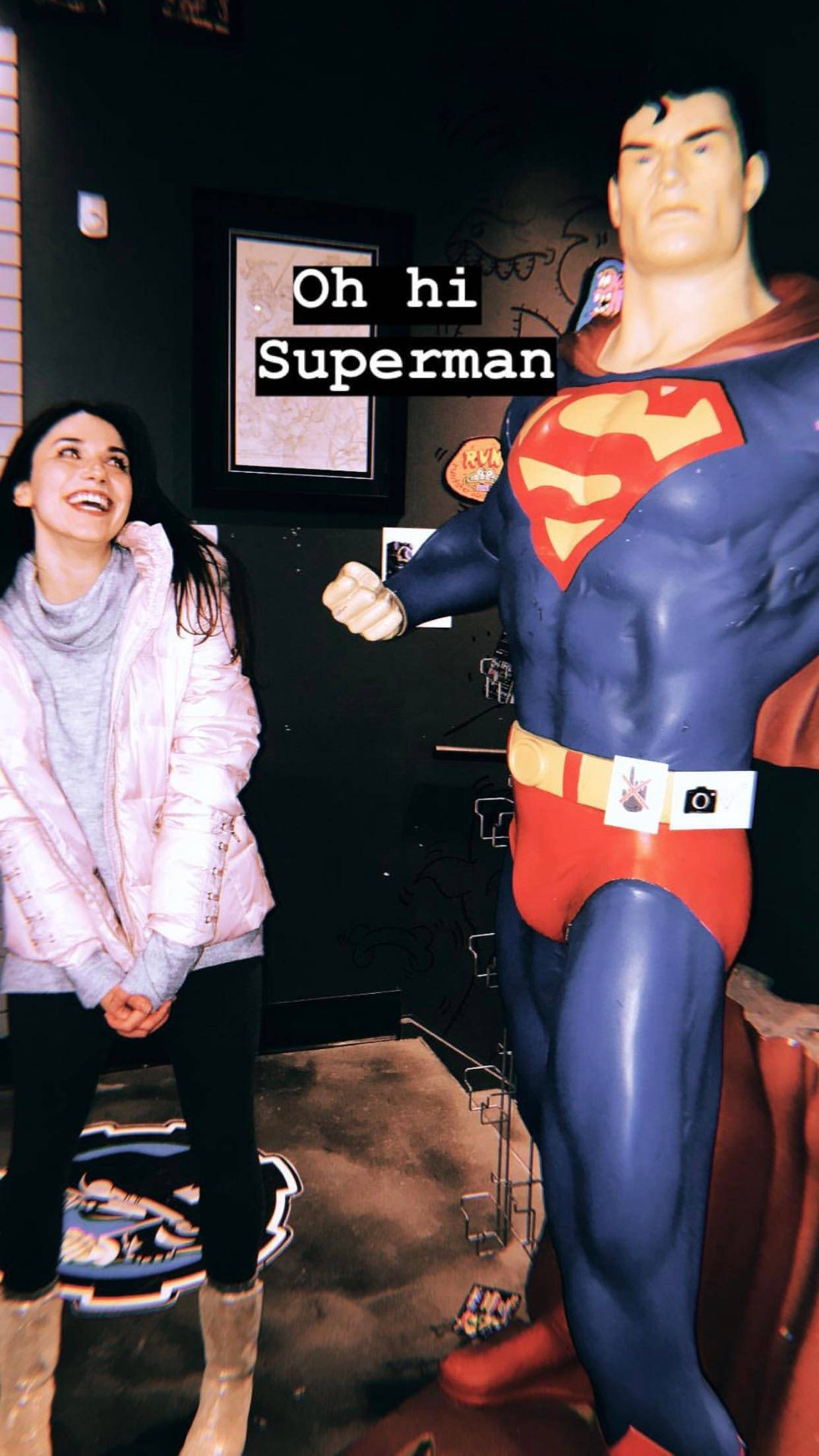 grace fulton 桌布 壁紙 — 一位女士在光線昏暗的室內空間中，在塗鴉牆旁與真人大小超人雕像旁邊大笑。