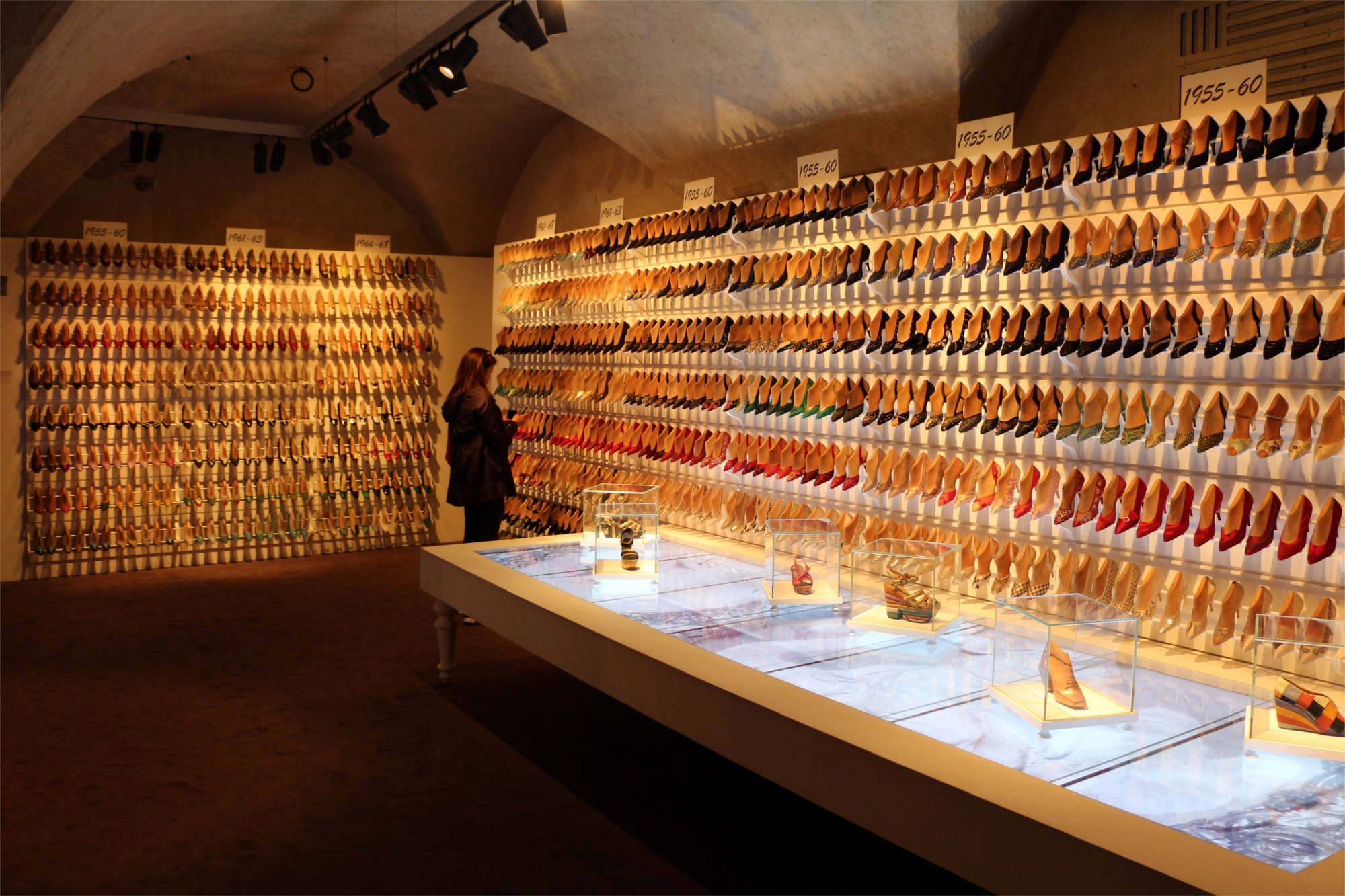 Ferragamo 桌布 壁紙 — 一位女士在博物館畫廊觀看按年代排列的復古鞋款大型照明牆展示。