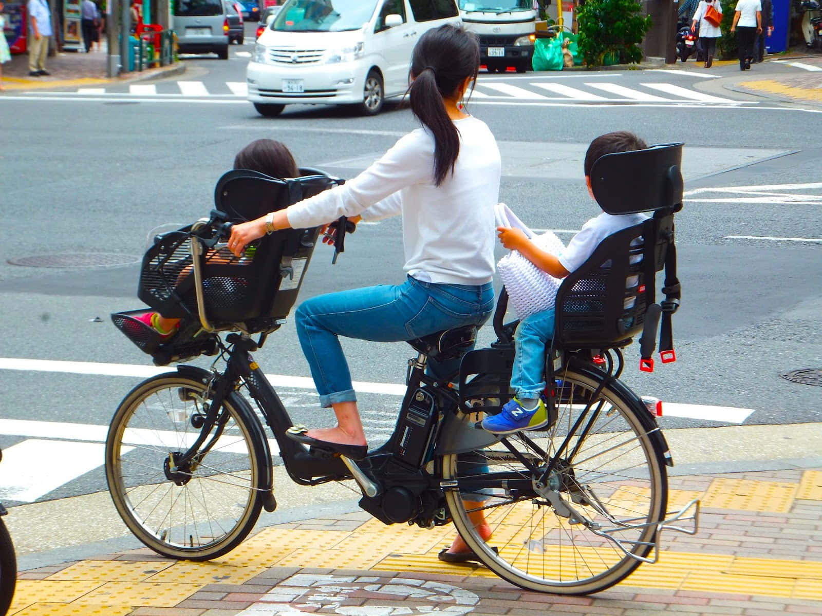 Bicycle 桌布 壁紙 — 一位女士在城市的街道上騎腳踏車，後座和前座兒童座椅上各固定了一名兒童。