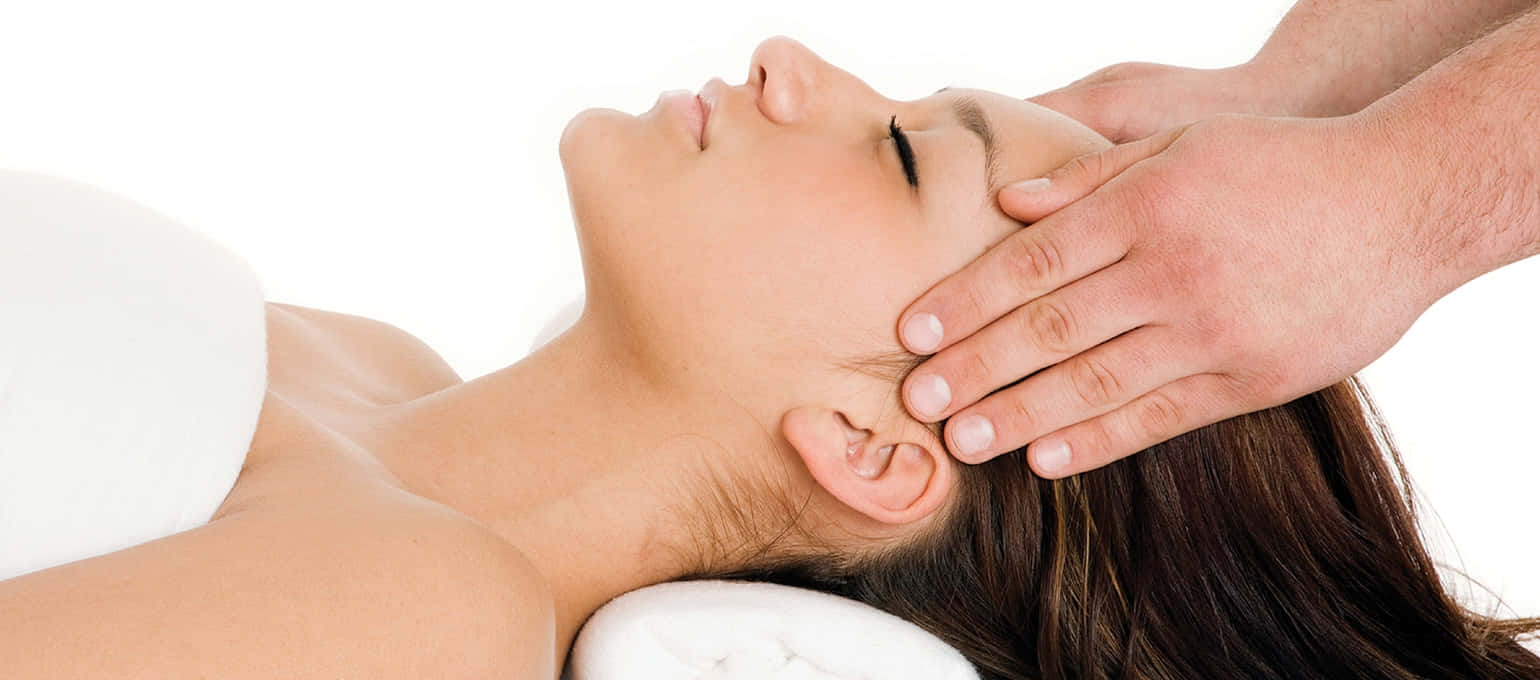 Massage 桌布 壁紙 — 一位女士在明亮的白色背景前接受舒緩的頭部按摩，雙手輕輕按壓她的太陽穴。