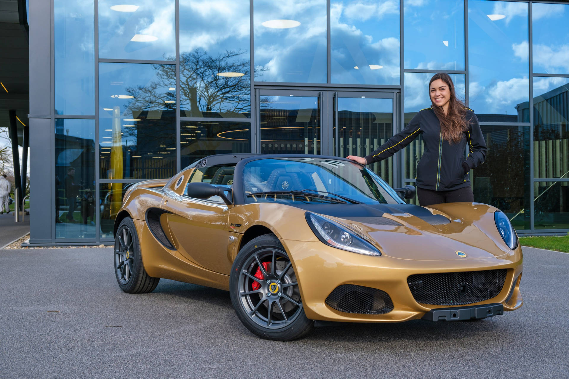 女士在玻璃建築前與金色跑車合影 — 4K 壁紙