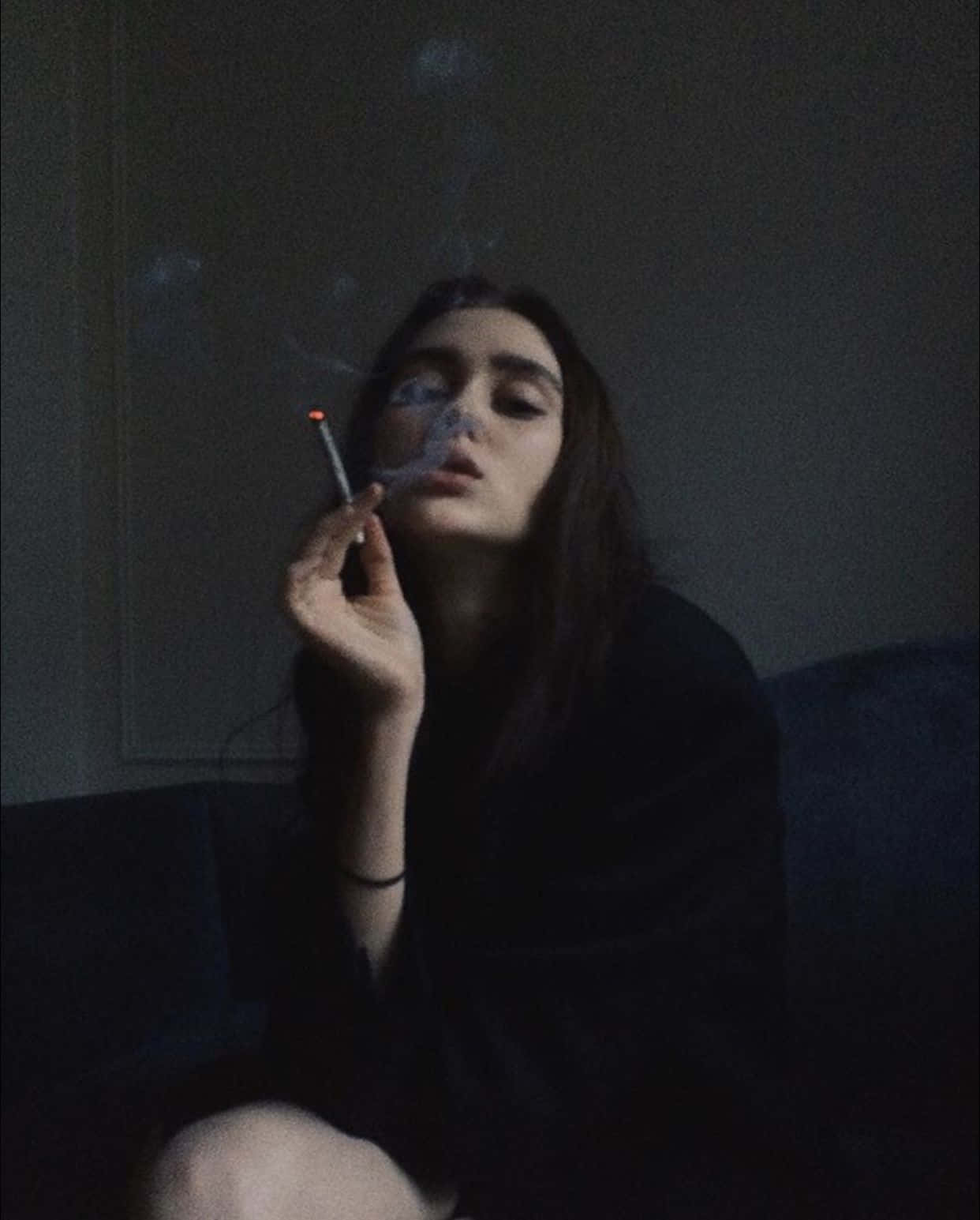 抽菸 桌布 壁紙 — 一位女士在昏暗的燈光下坐在沙發上抽煙，煙霧在她臉龐縈繞。