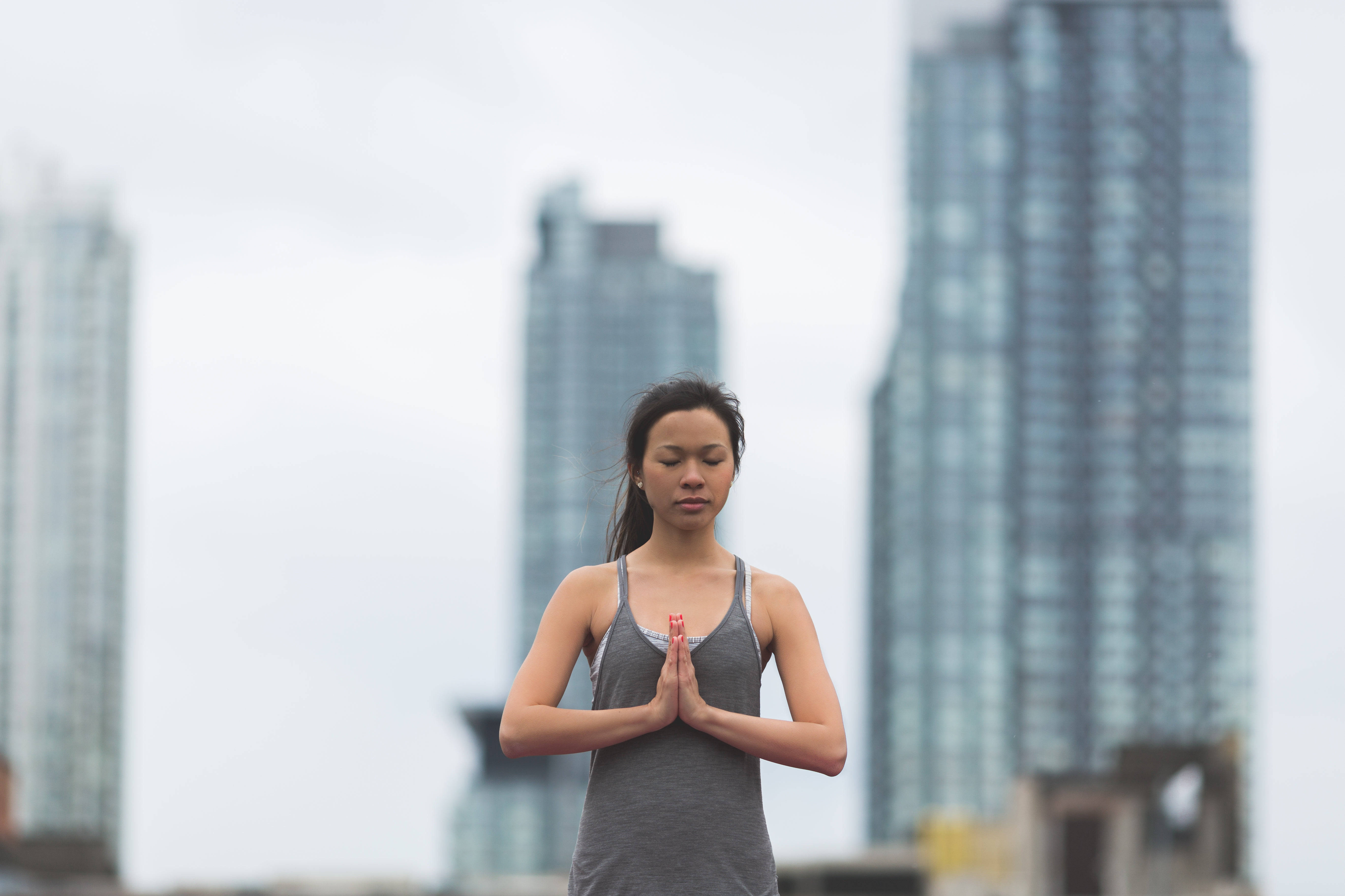 Skyscraper 桌布 壁紙 — 一位女士在模糊的城市摩天大樓背景下，雙手合十於身前，平靜地冥想。