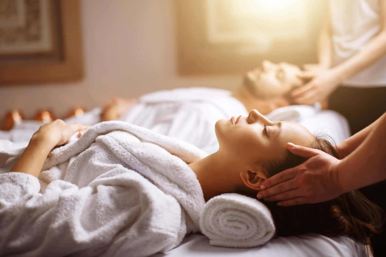 Massage 桌布 壁紙 — 一位女士在水療中心放鬆，享受舒緩的頭部按摩，柔和陽光透過窗戶灑入。
