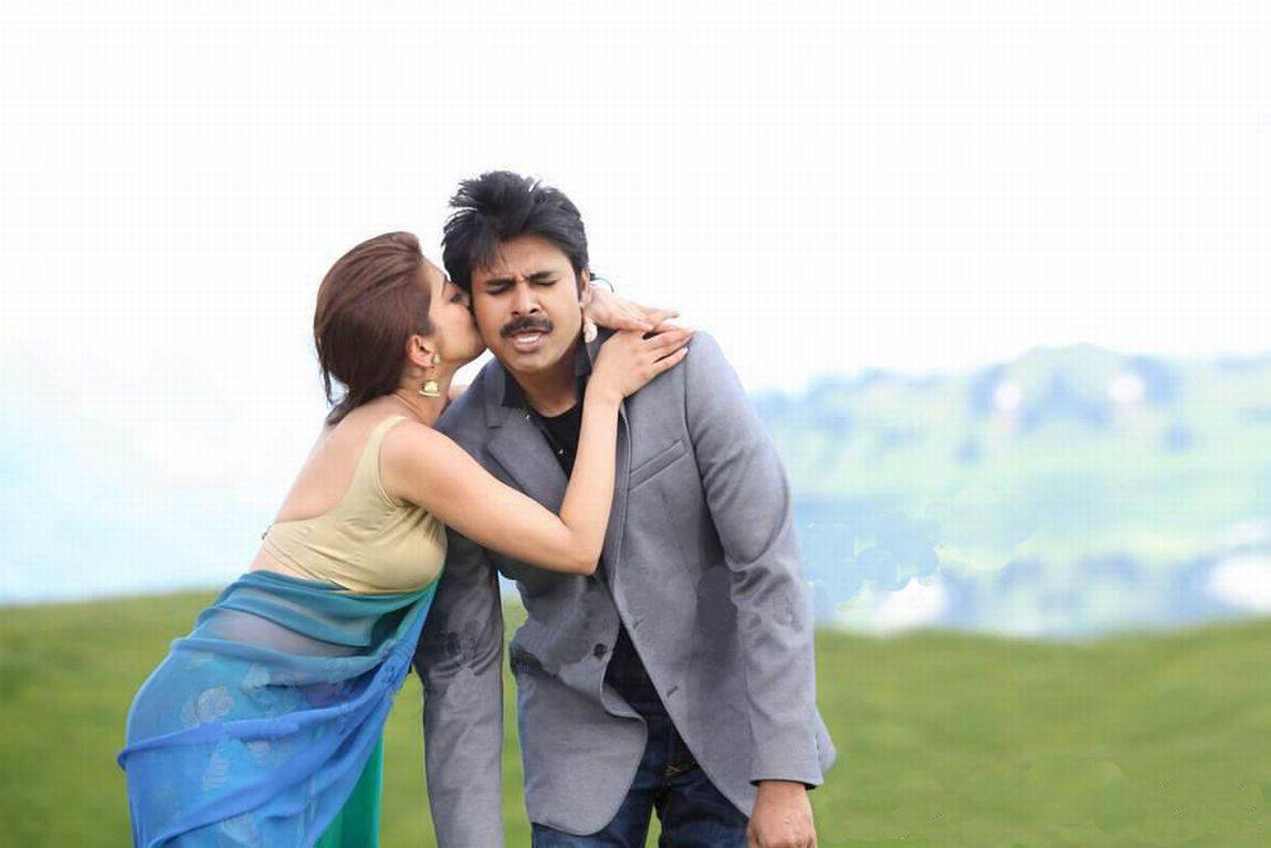 Pawan Kalyan 桌布 壁紙 — 一位女士在草地上親吻男士的臉頰，背景是起伏的丘陵。