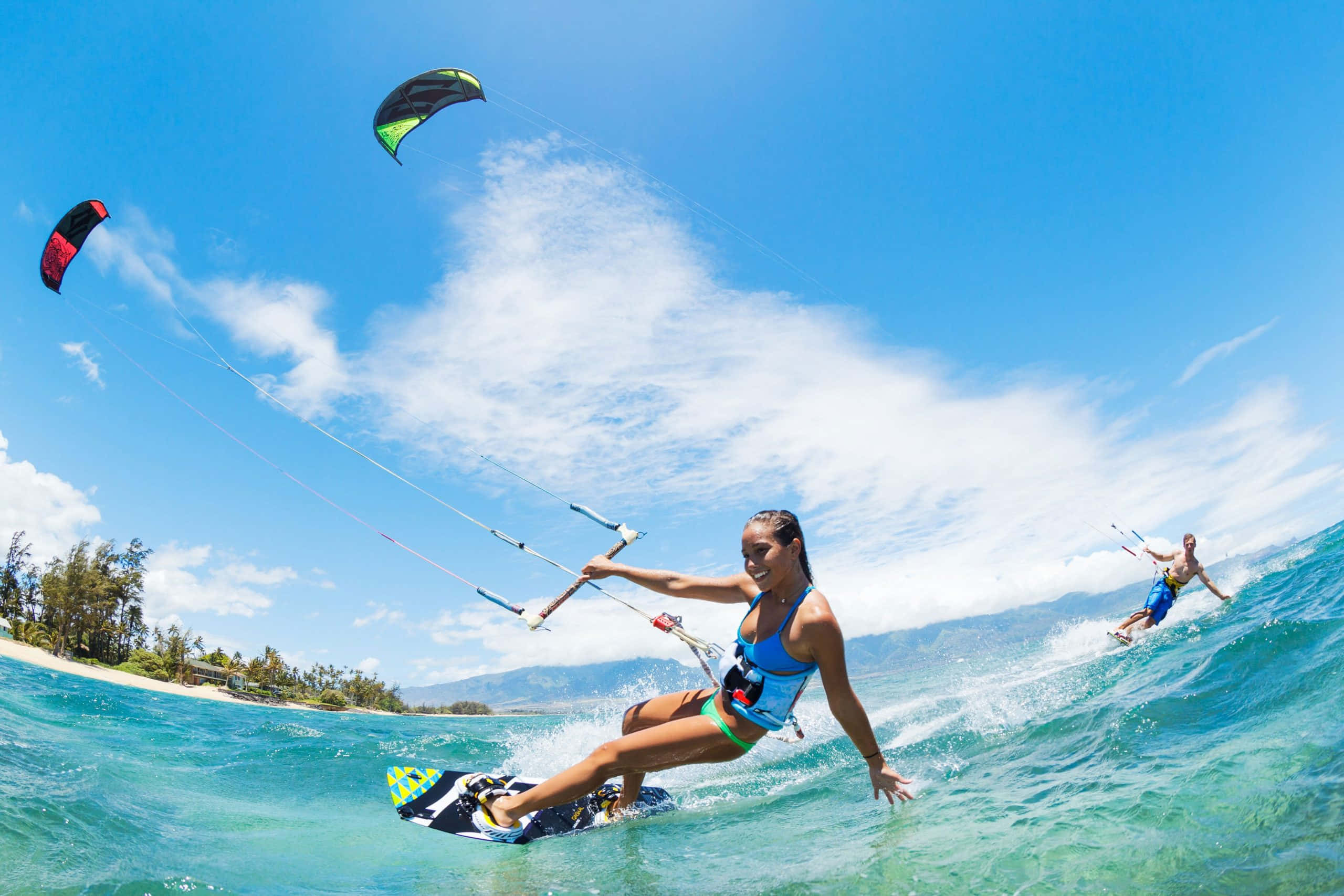 Beach Water Sports 桌布 壁紙 — 一位女士在蔚藍的波浪上風箏衝浪，微笑著，頭上是明亮的藍天和蓬鬆的雲朵。