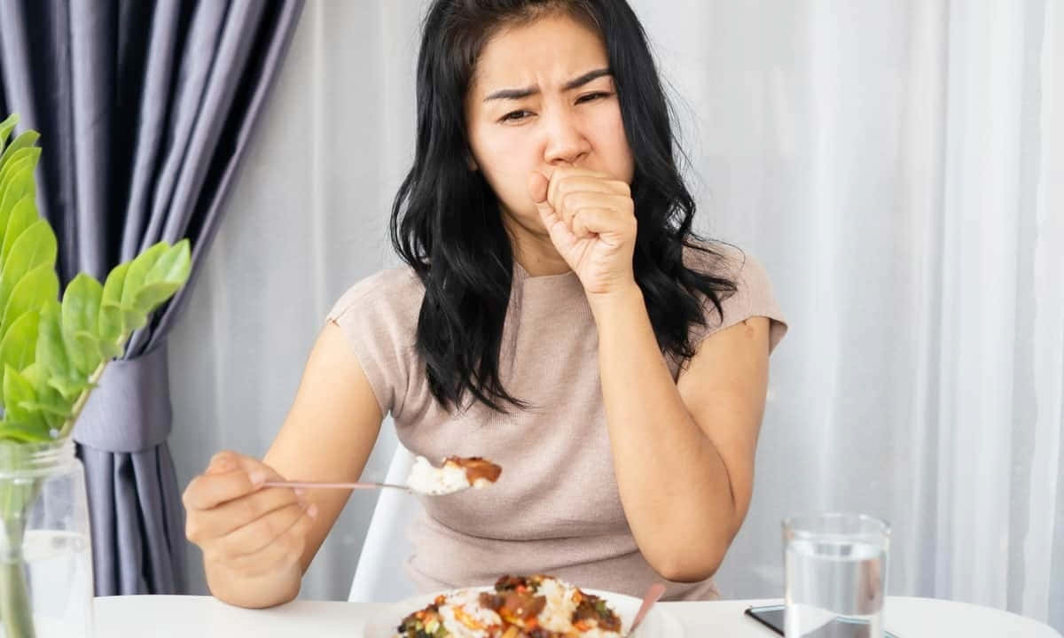 生病 桌布 壁紙 — 一位女士在餐桌上拿著一匙食物，同時做鬼臉並捂住嘴巴。