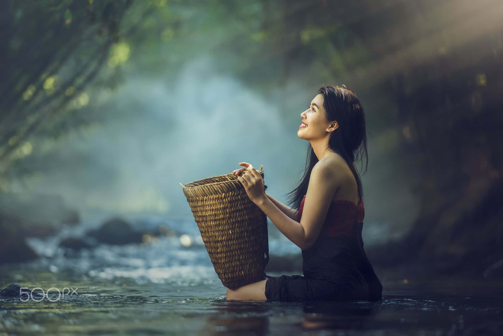 森林 桌布 壁紙 — 一位女士坐在霧氣瀰漫的森林溪流中，手持編織籃，平靜地微笑。