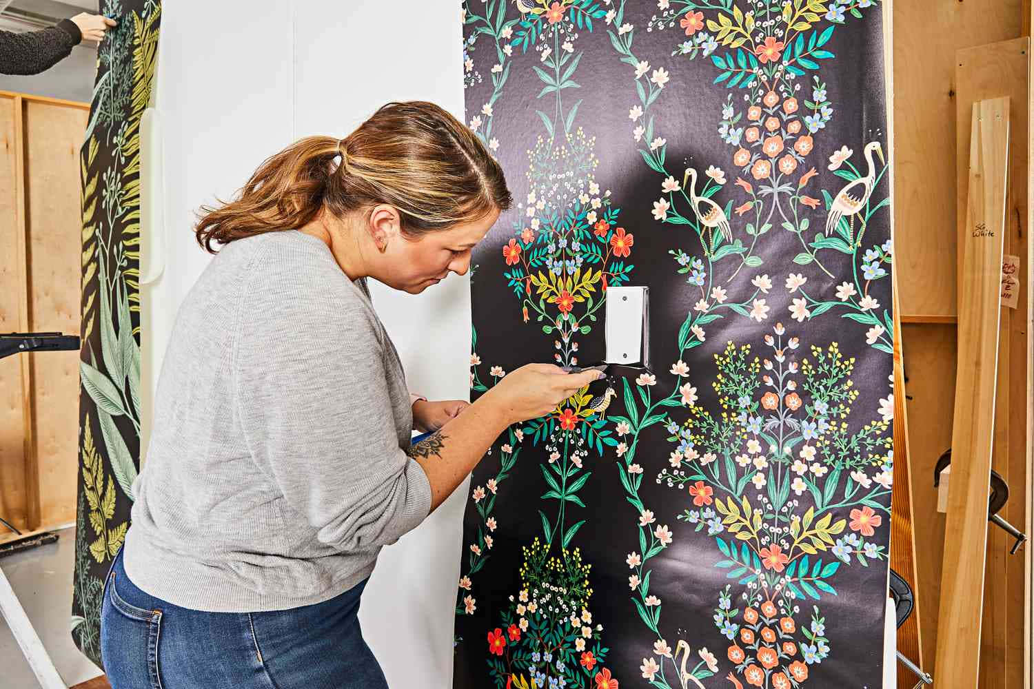 Walls 桌布 壁紙 — 一位女士小心地將帶有火鶴的鮮豔花卉壁紙貼在木框房間的牆上。