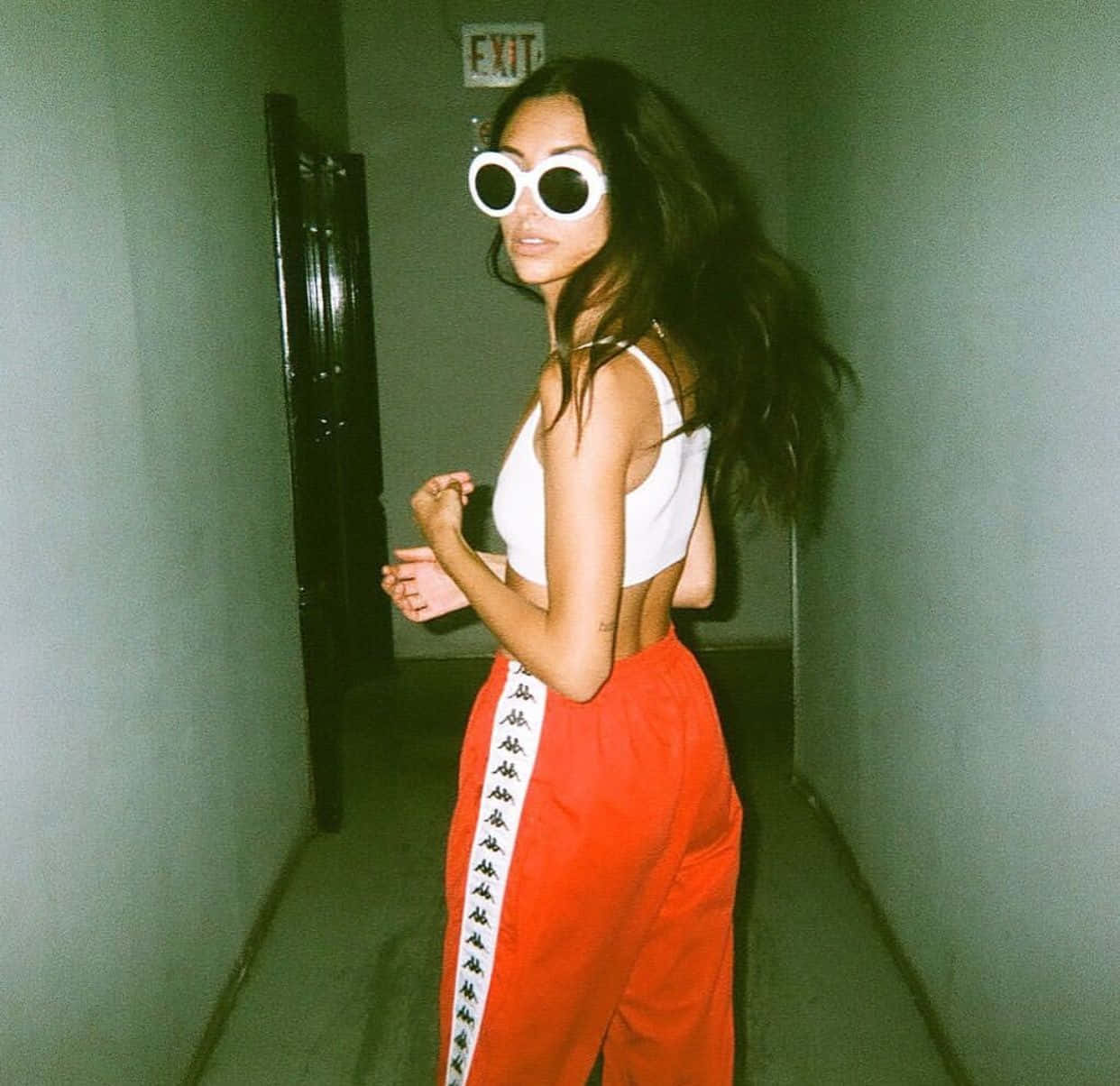 Baddie Vintage 90's Aesthetic 桌布 壁紙 — 一位女士戴著超大白框太陽眼鏡和鮮紅色運動褲，在昏暗的走廊中自信地擺姿勢。