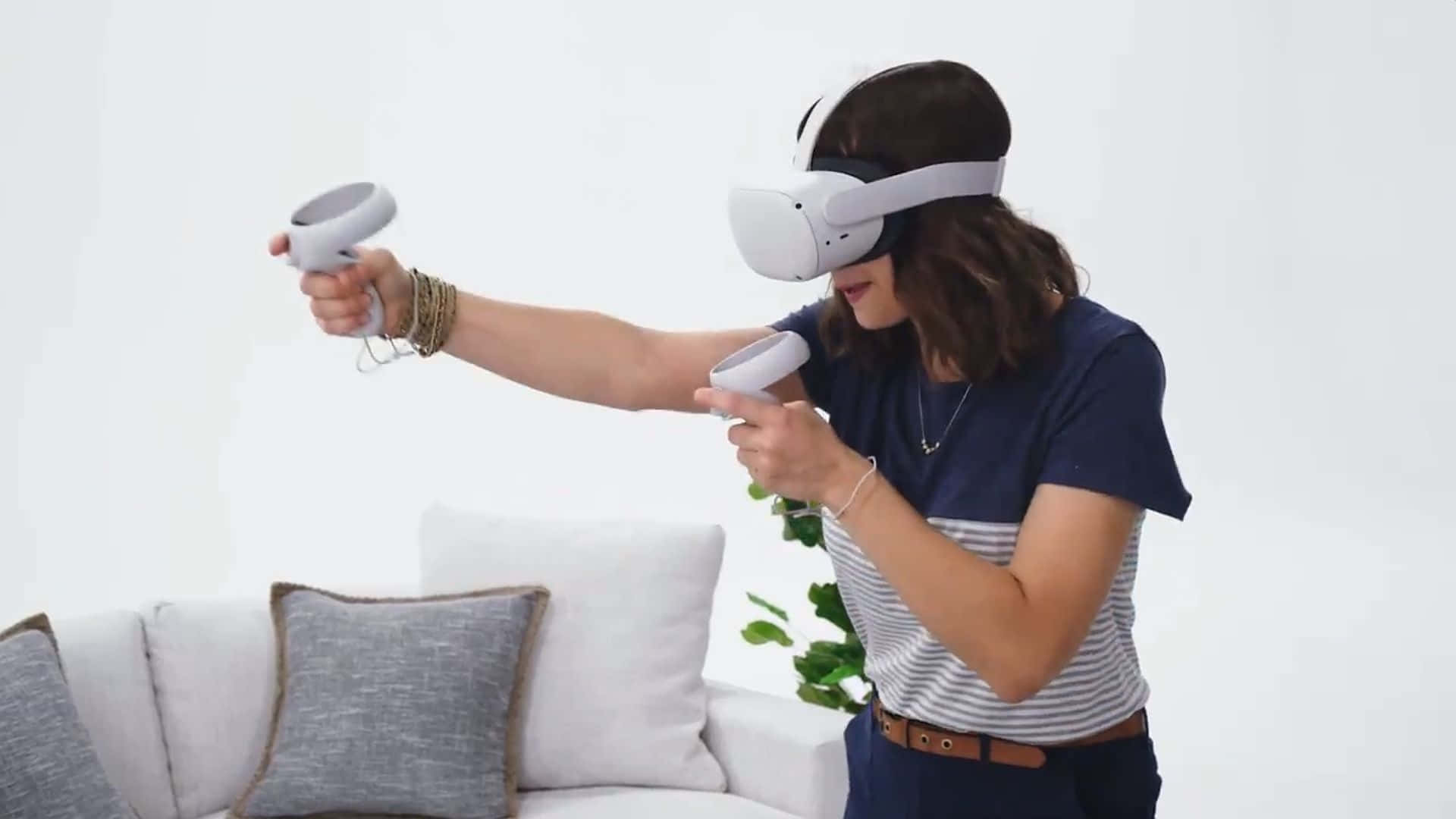 Oculus Quest 2 桌布 壁紙 — 一位女士手持控制器沉浸在虛擬實境中，站在一個簡約的客廳裡，客廳內有白色沙發和綠色植物。