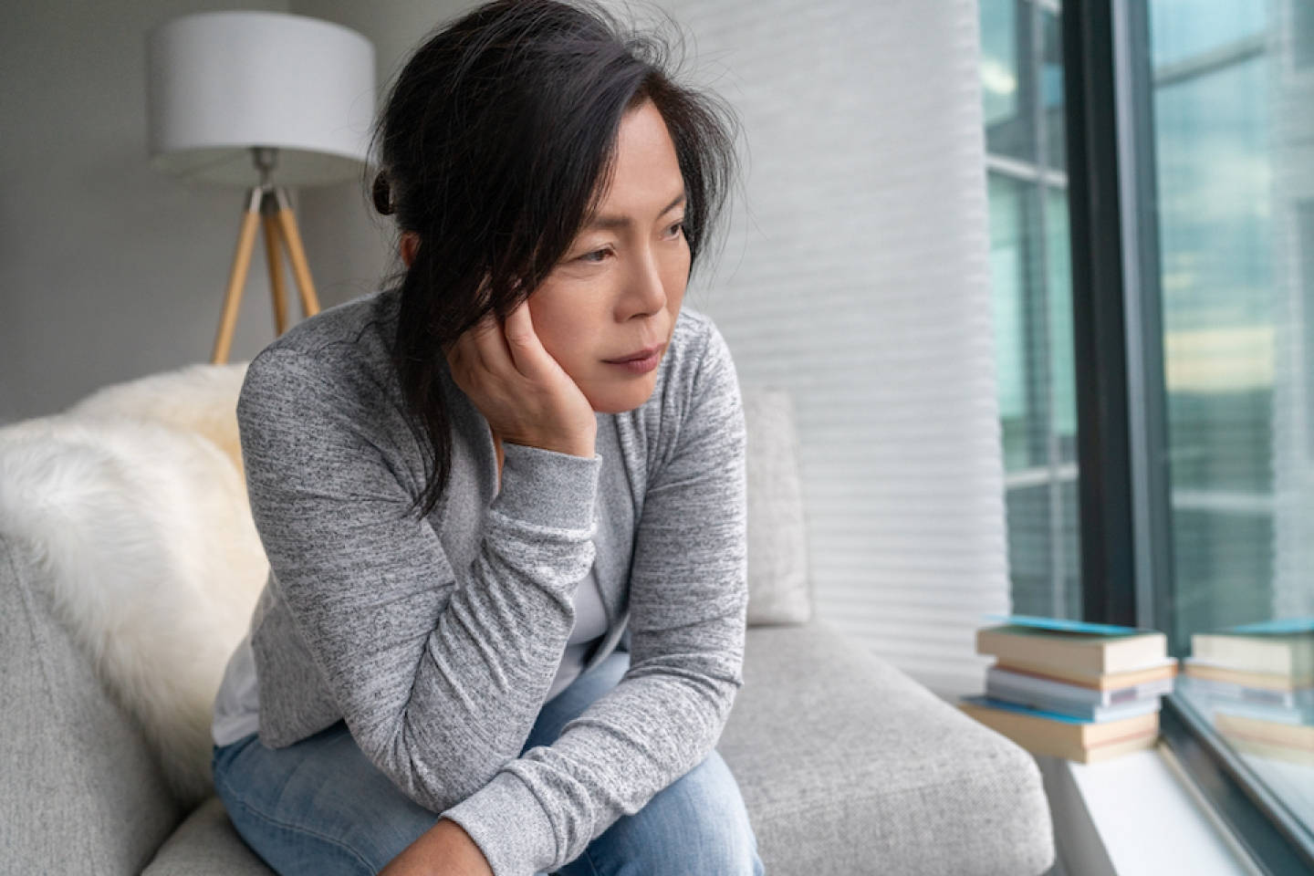 anxious 桌布 壁紙 — 一位女士沉思地坐在灰色沙發上，手托著臉頰，望向窗外城市景觀。