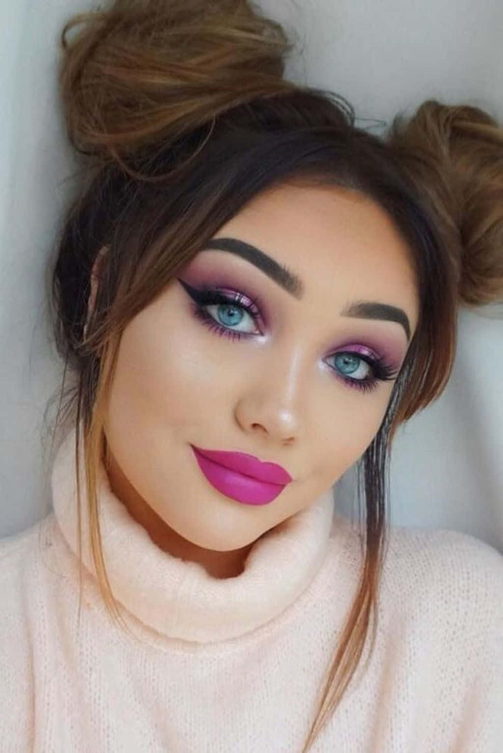 Spring Makeup 桌布 壁紙 — 一位女士的近距離肖像，塗著大膽的紫色唇膏和戲劇性的眼妝，穿著柔軟的粉紅色高領毛衣，微笑著。