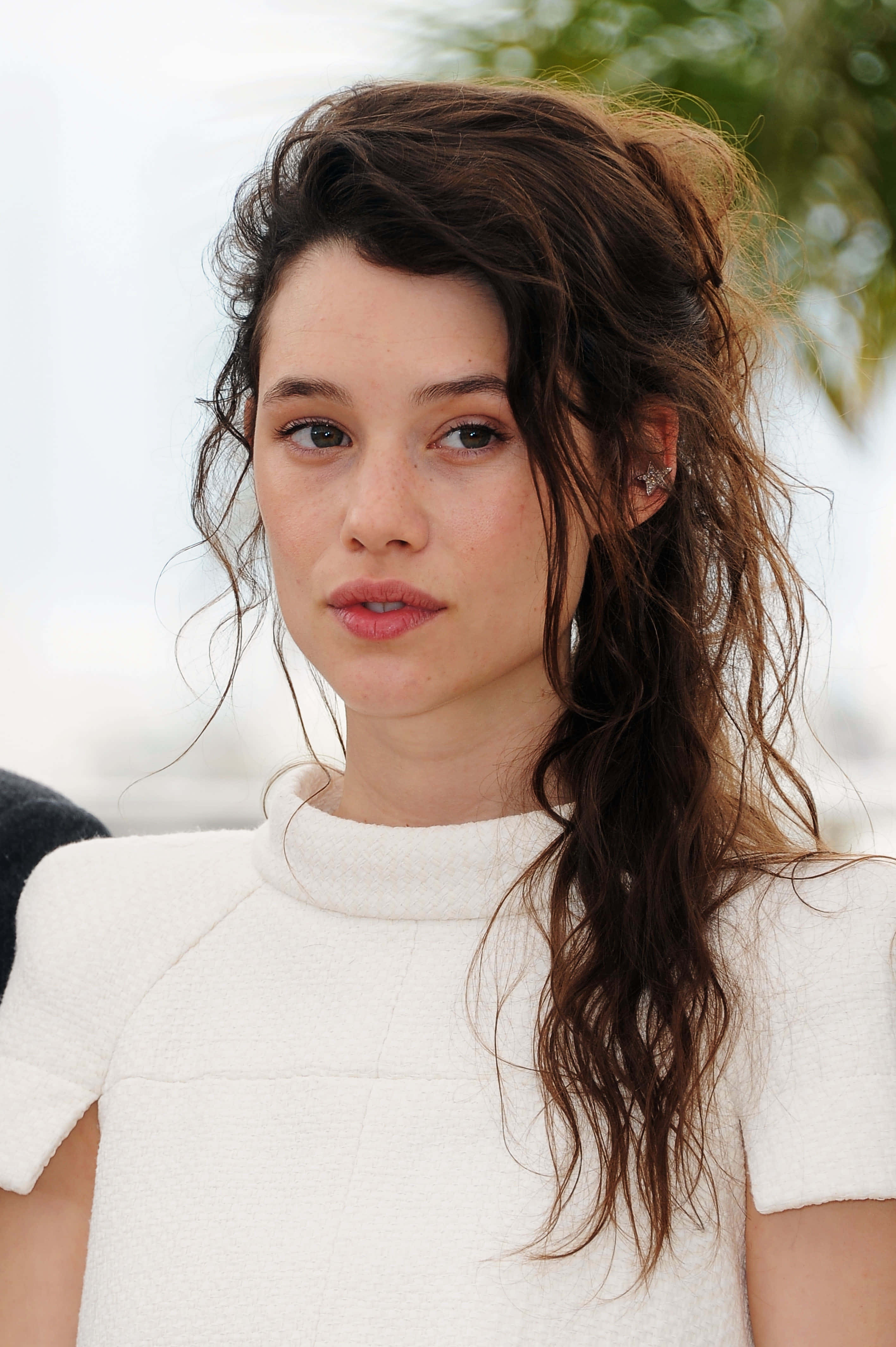 Astrid Berges Frisbey 桌布 壁紙 — 一位女士的近距離肖像照，她有一頭凌亂的棕色頭髮，穿著白色質感上衣，背景是明亮的戶外。